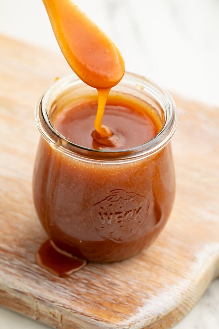 A spoonful of caramel sauce being lifted out of a glass jar of caramel sauce.