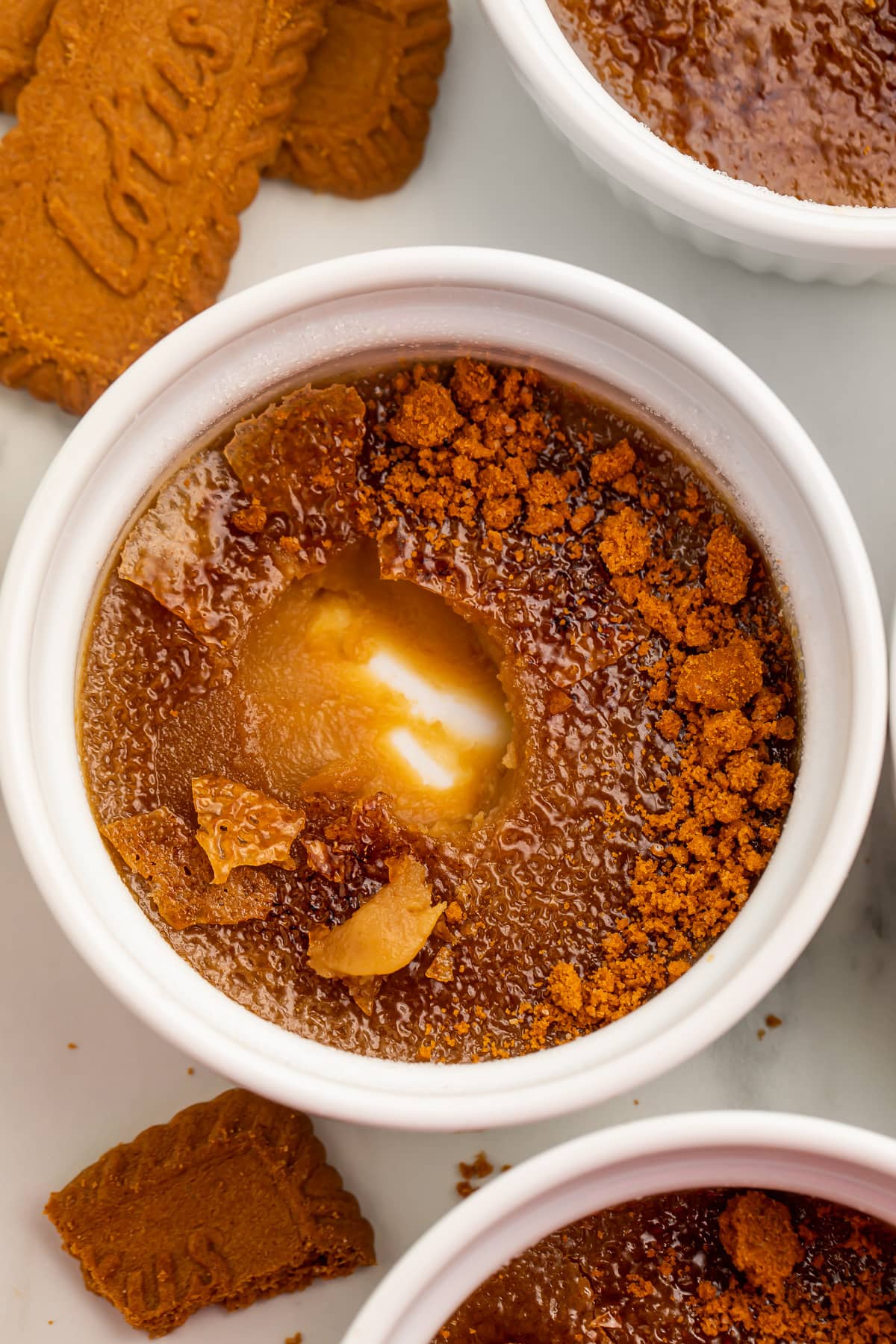Biscoff cookie butter creme brulee in a round white ramekin with one spoonful missing from the center, showing the bottom of the ramekin.