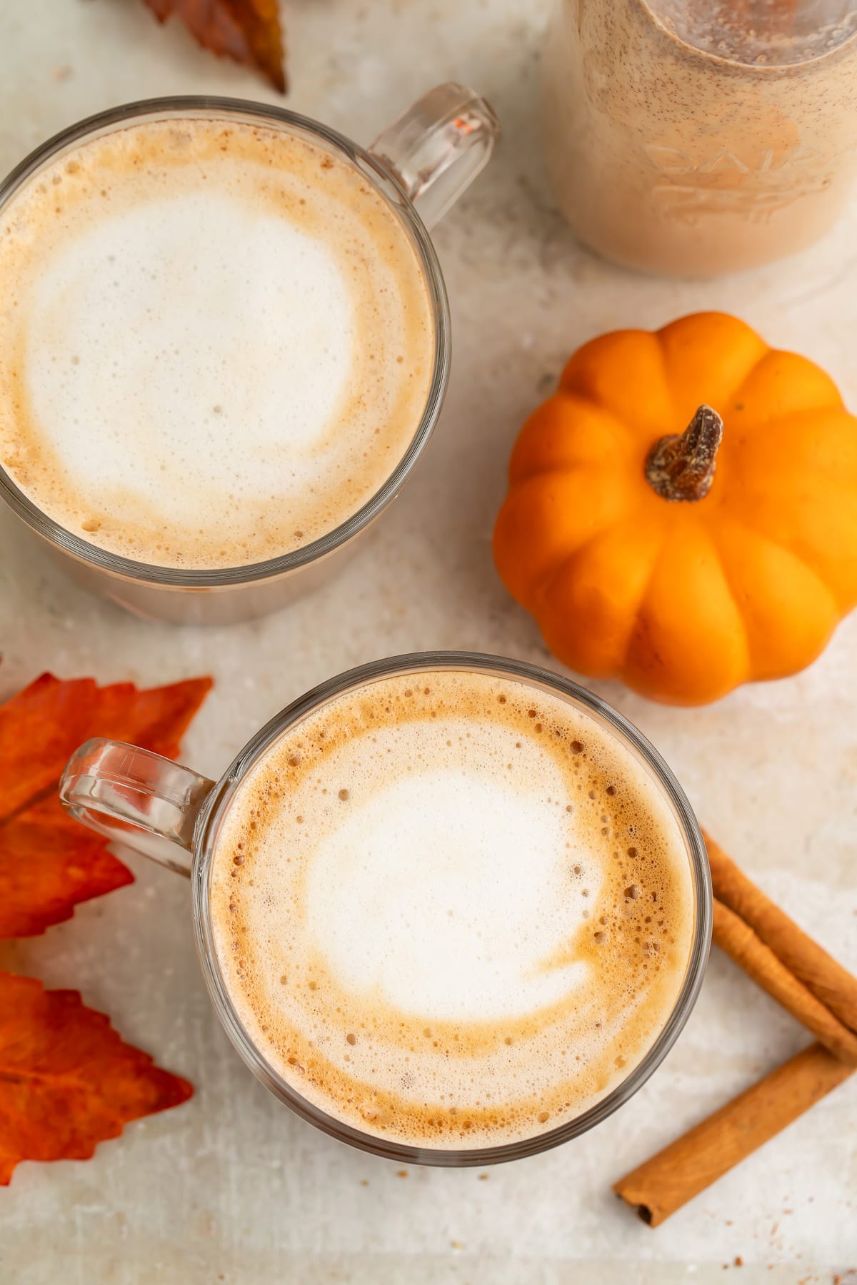 Overhead view of two clear glass coffee mugs holding a pumpkin spice latte with rich pumpkin spice creamer.