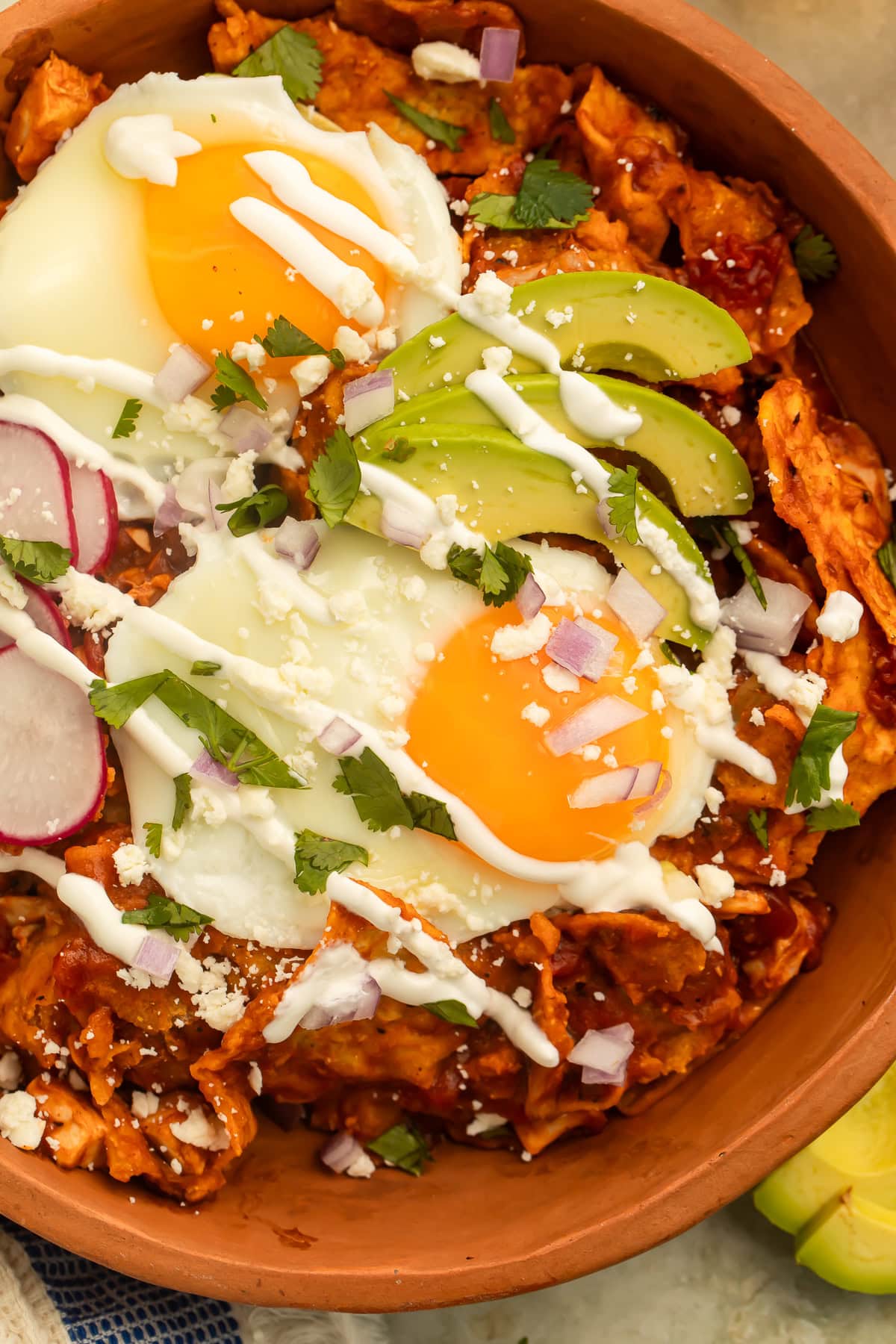 Two fried eggs, sliced avocado and cilantro on top of a bowl of Chilaquiles.