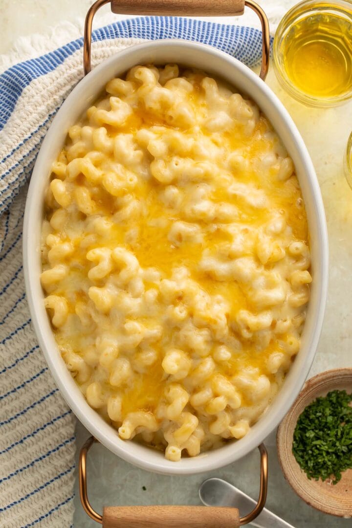 Overhead view of a large oval casserole dish holding a rich, creamy truffle mac and cheese on a table with a glass of white wine and a blue striped napkin.