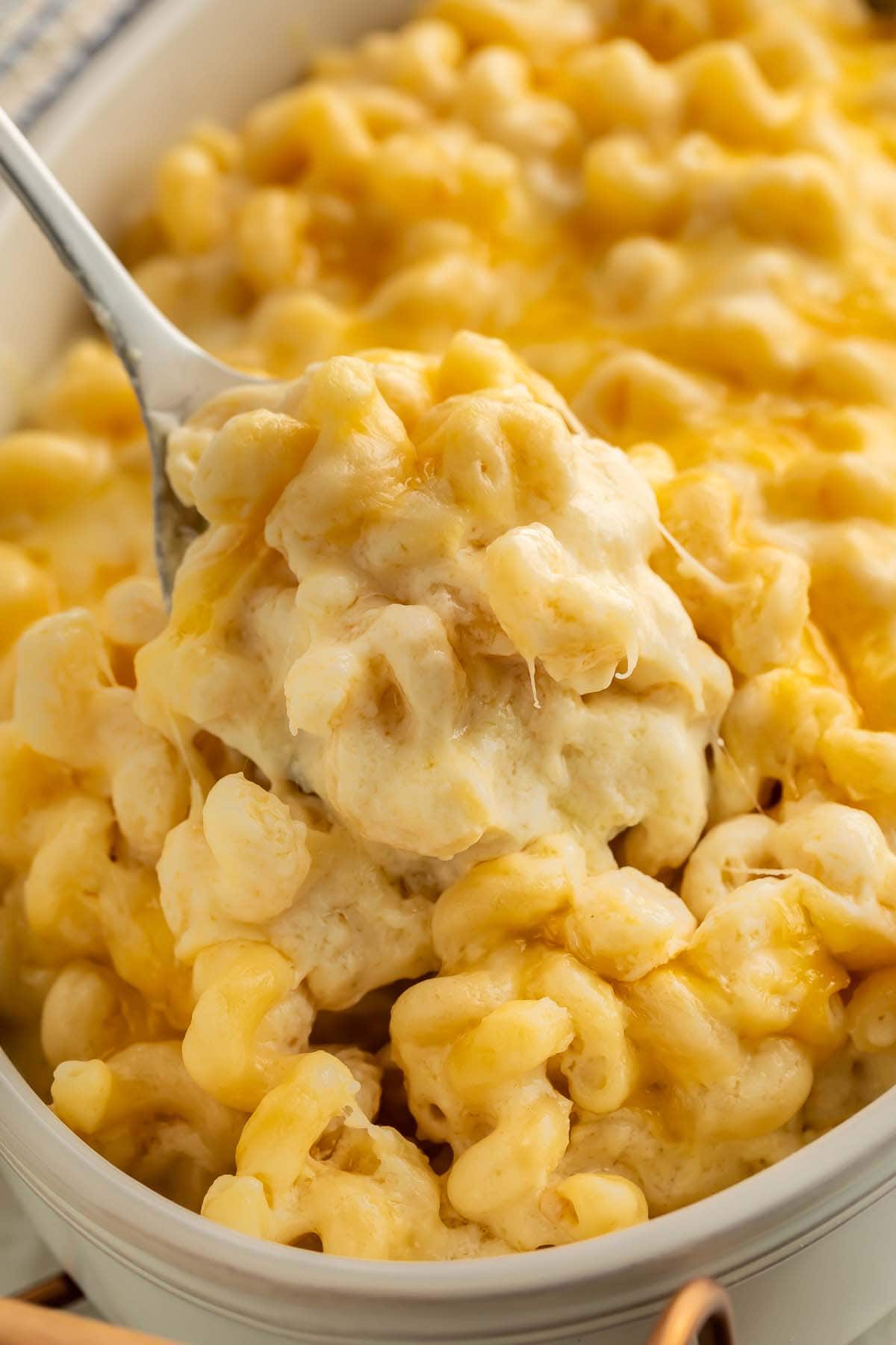 A scoop of truffle mac and cheese being held up over a casserole dish by a large silver spoon.