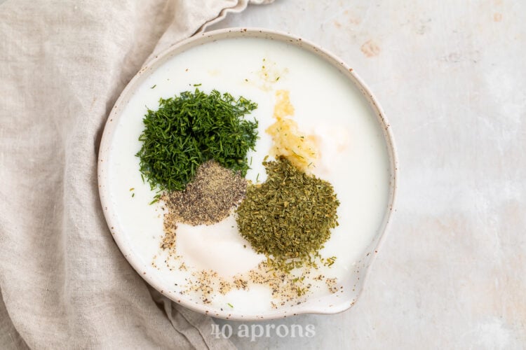 Overhead view of ranch dressing ingredients in a medium white mixing bowl on a neutral cloth napkin.