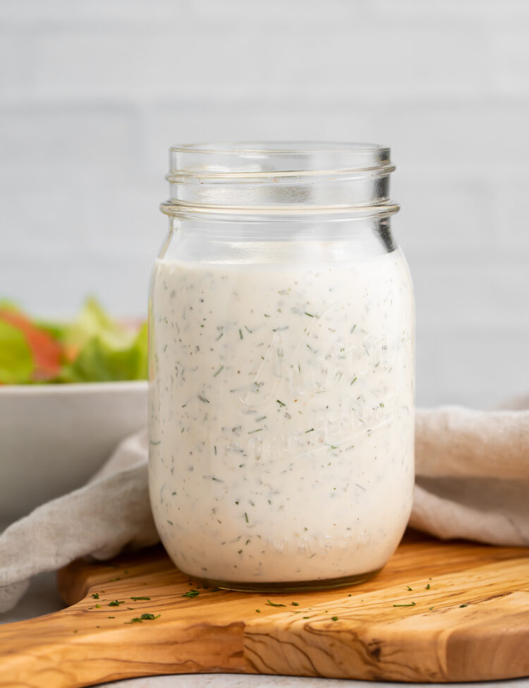 Side view of a mason jar filled with homemade buttermilk ranch dressing, sitting on a wooden serving board.