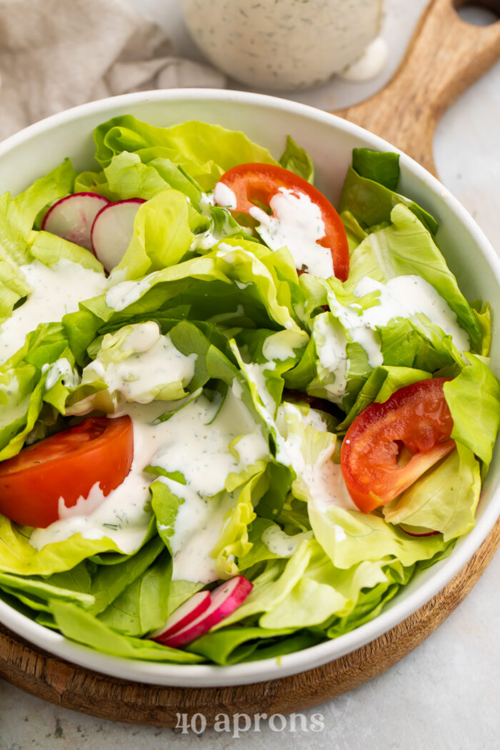 Overhead, angled view of a house salad with buttermilk ranch dressing and large slices of tomatoes.