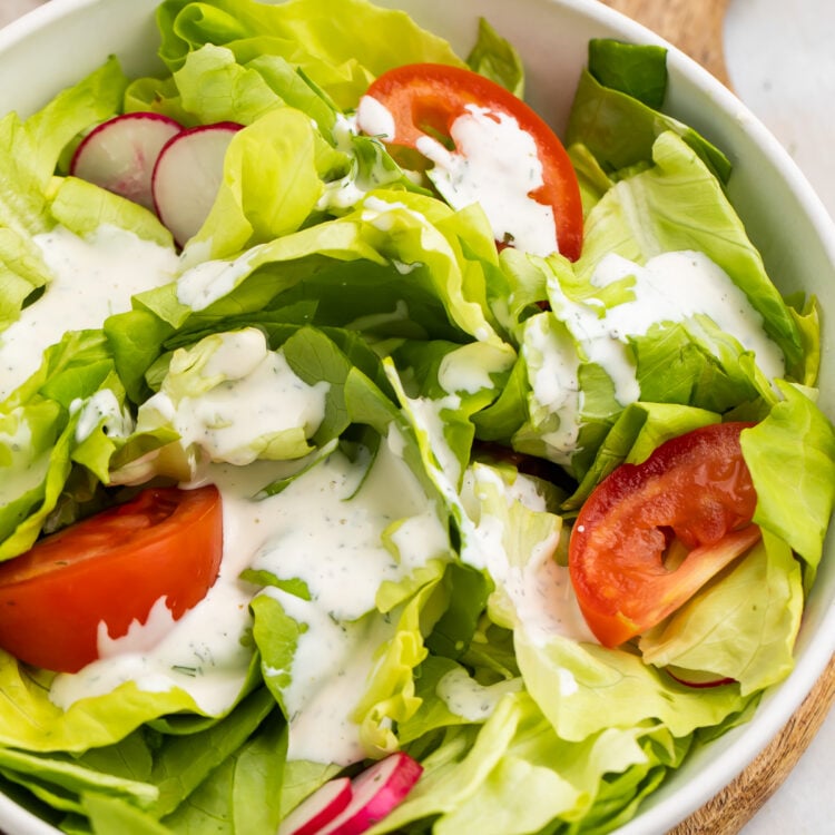 Overhead, angled view of a house salad with buttermilk ranch dressing and large slices of tomatoes.