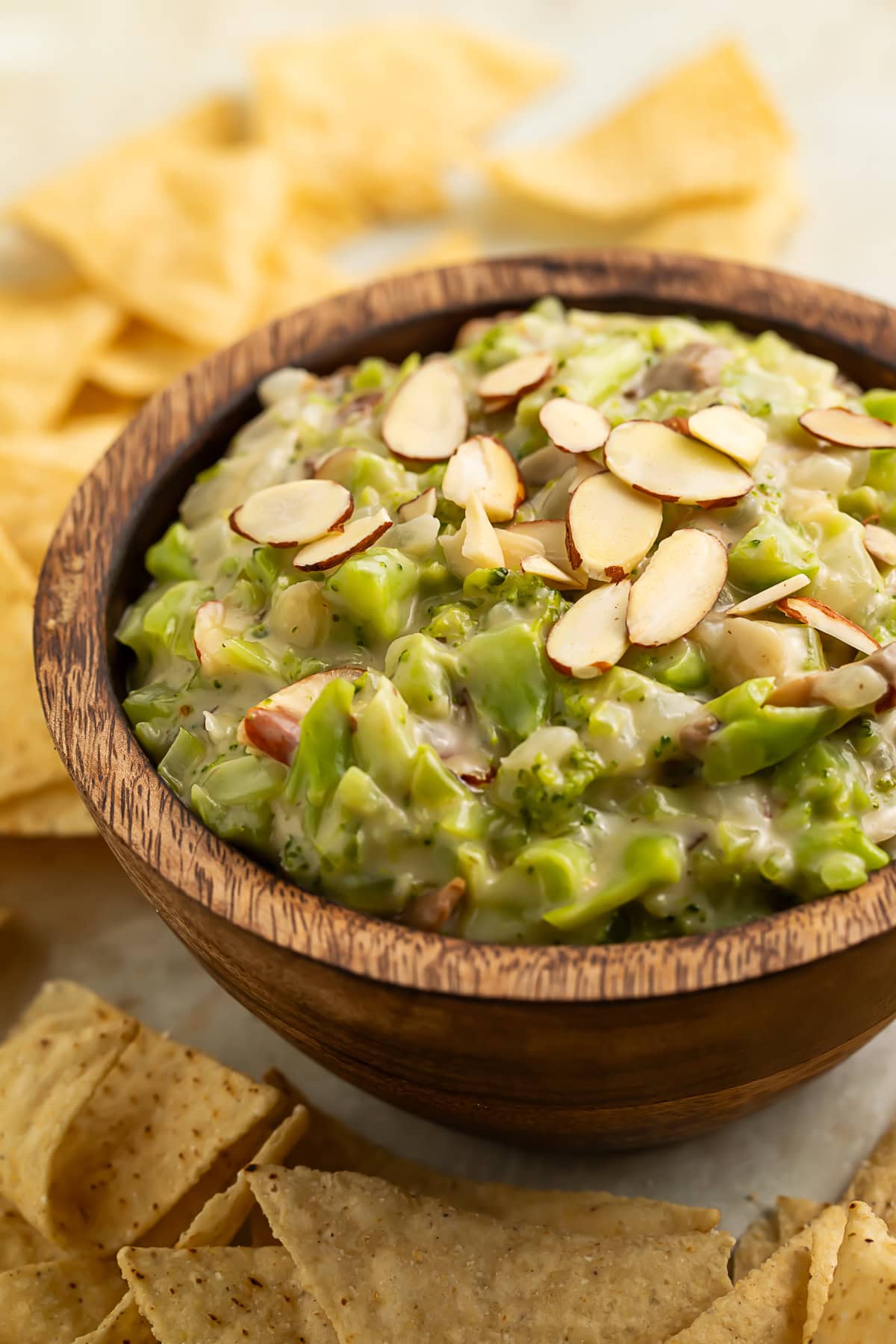 Wooden bowl of broccoli dip topped with sliced mushrooms with tortilla chips on the side.