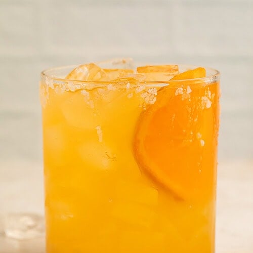 Clementine margarita on the rocks in a glass with an orange slice and a salt rim.