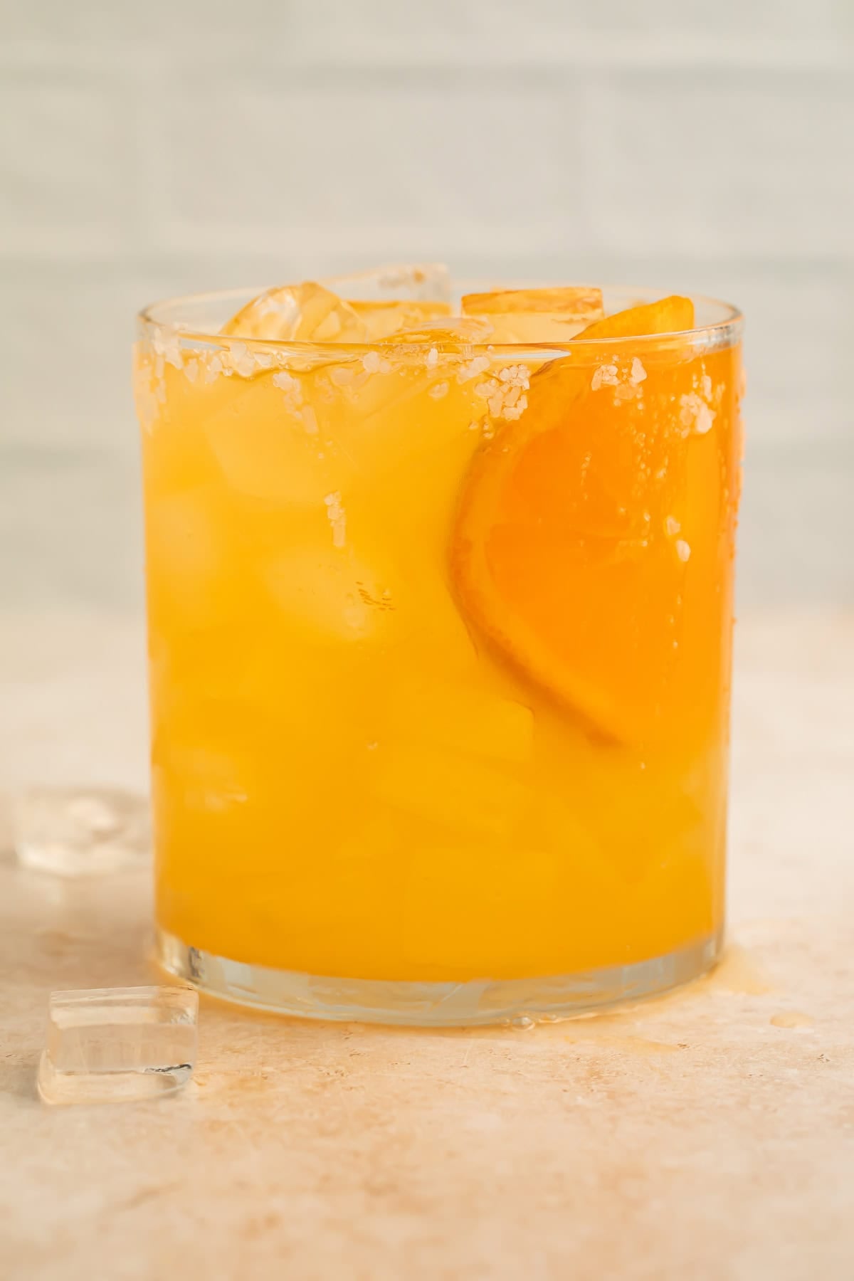 Clementine margarita on the rocks in a glass with an orange slice and a salt rim.
