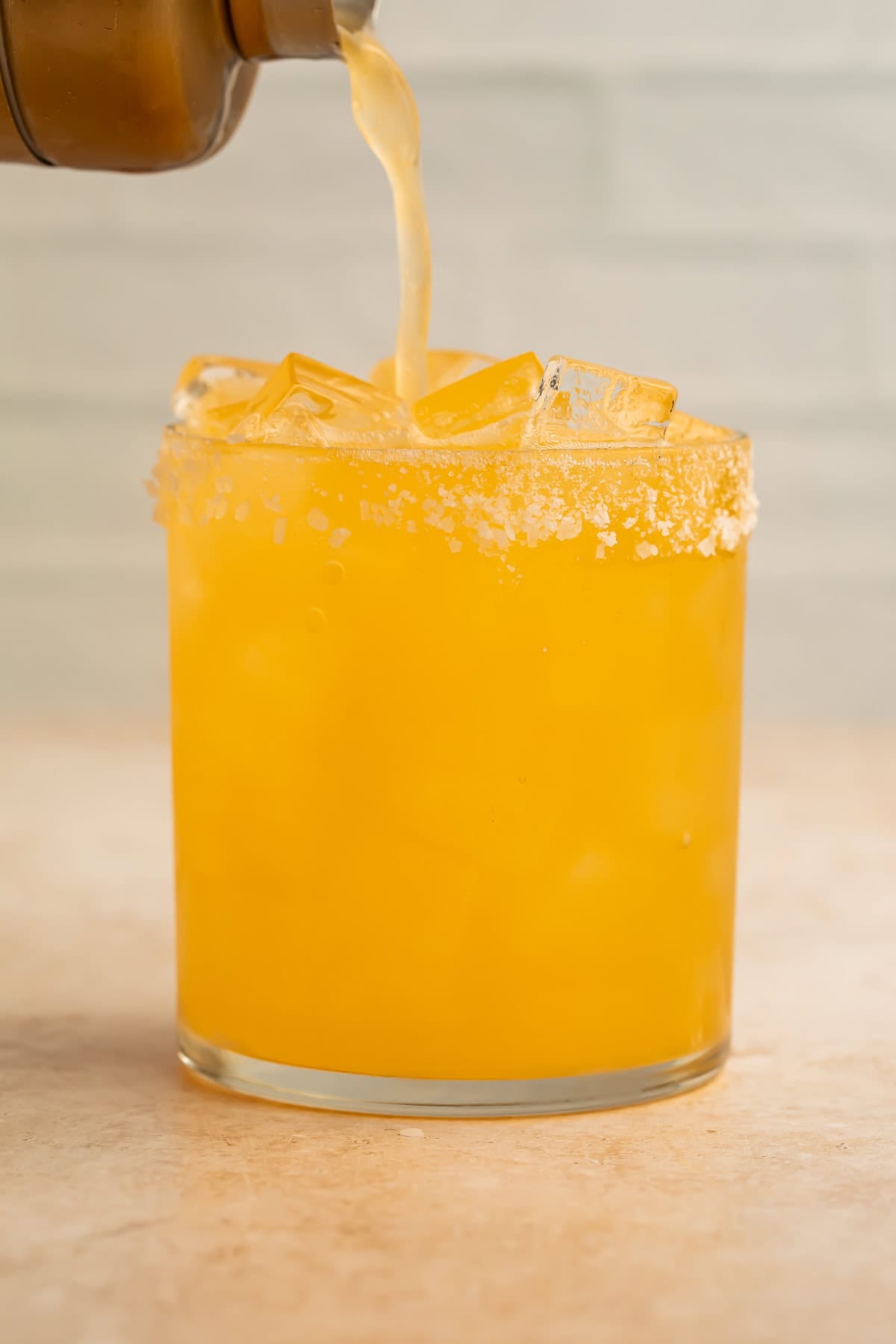 Clementine margarita being poured into a glass of ice from a copper cocktail shaker.
