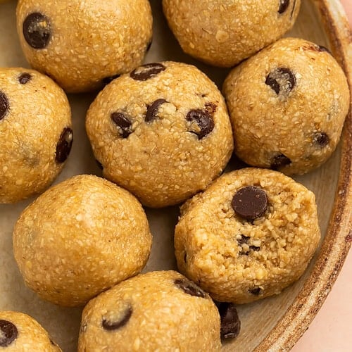 Close up of a plate of chocolate chip cookie dough energy balls with one missing a bite.