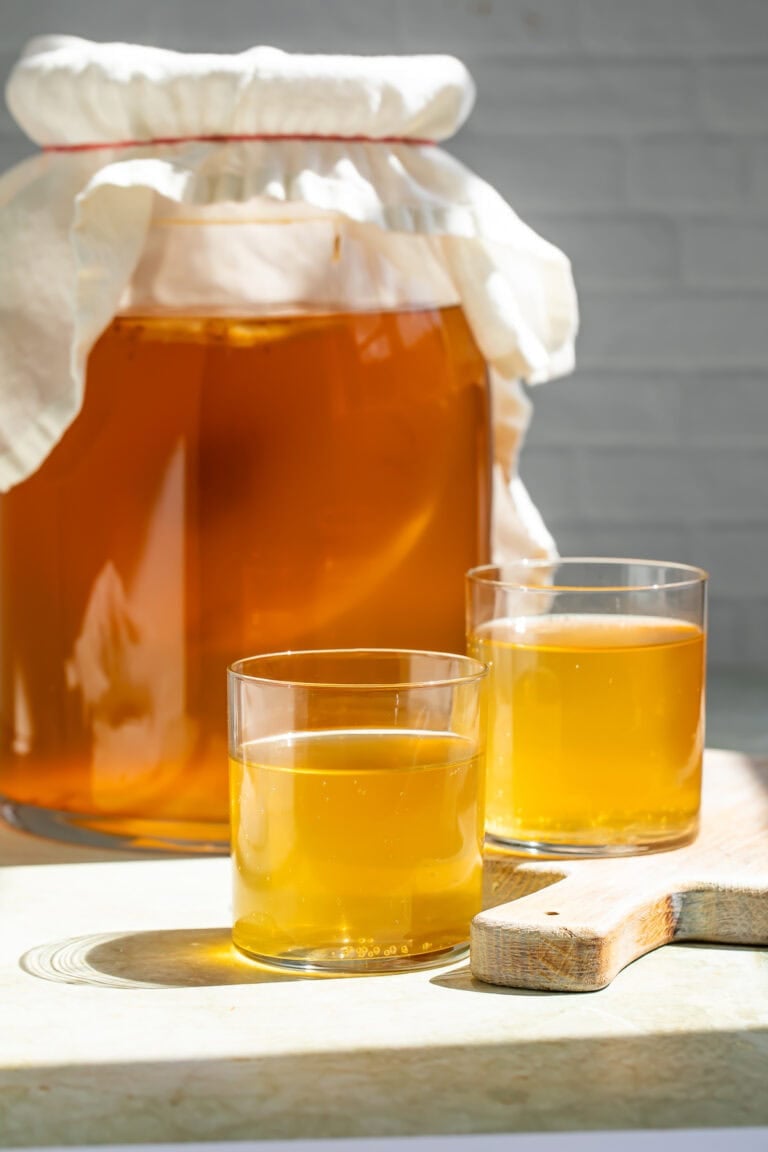 Jar of kombucha and SCOBY with two glasses of kombucha in the foreground.