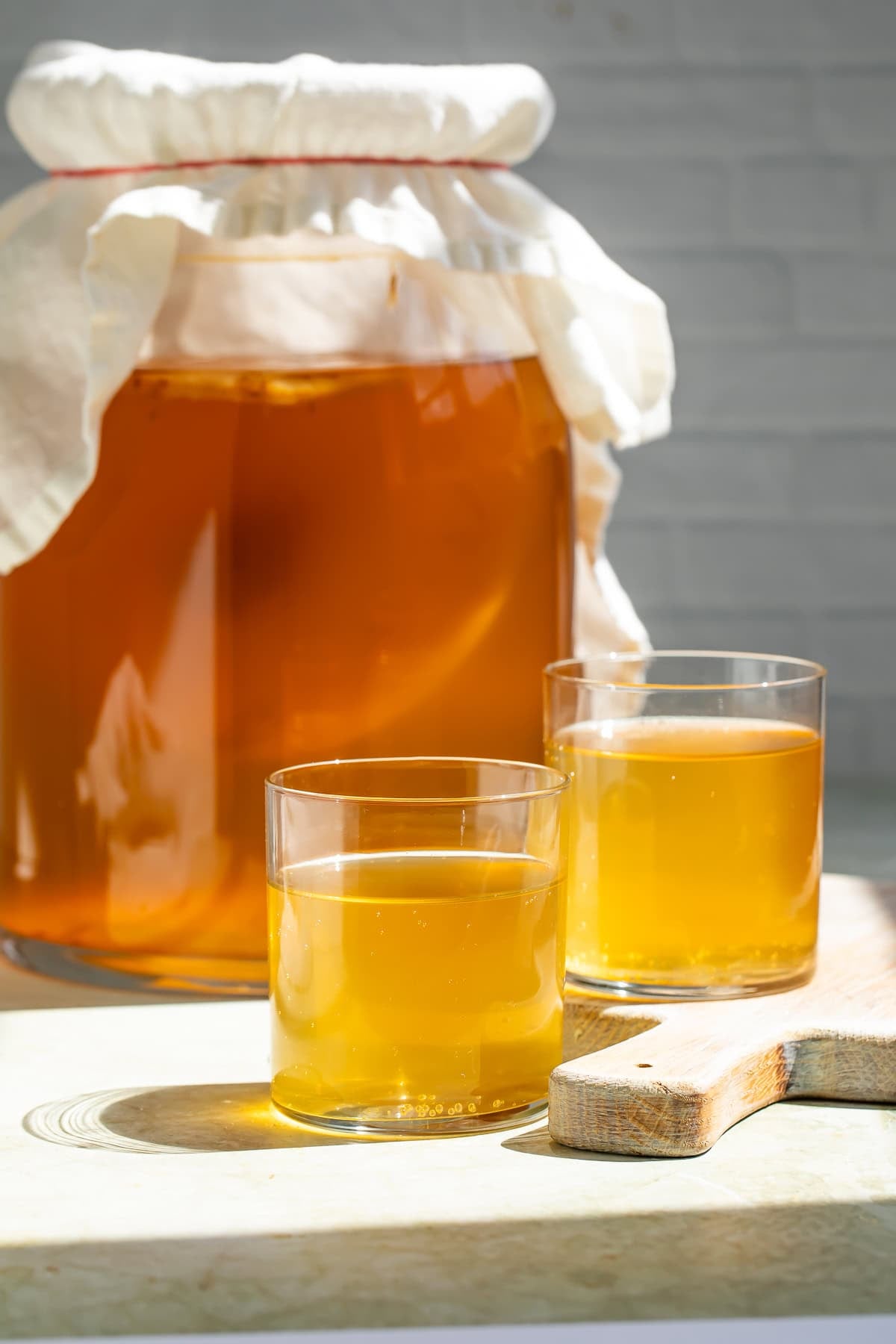 Jar of kombucha and SCOBY with two glasses of kombucha in the foreground.