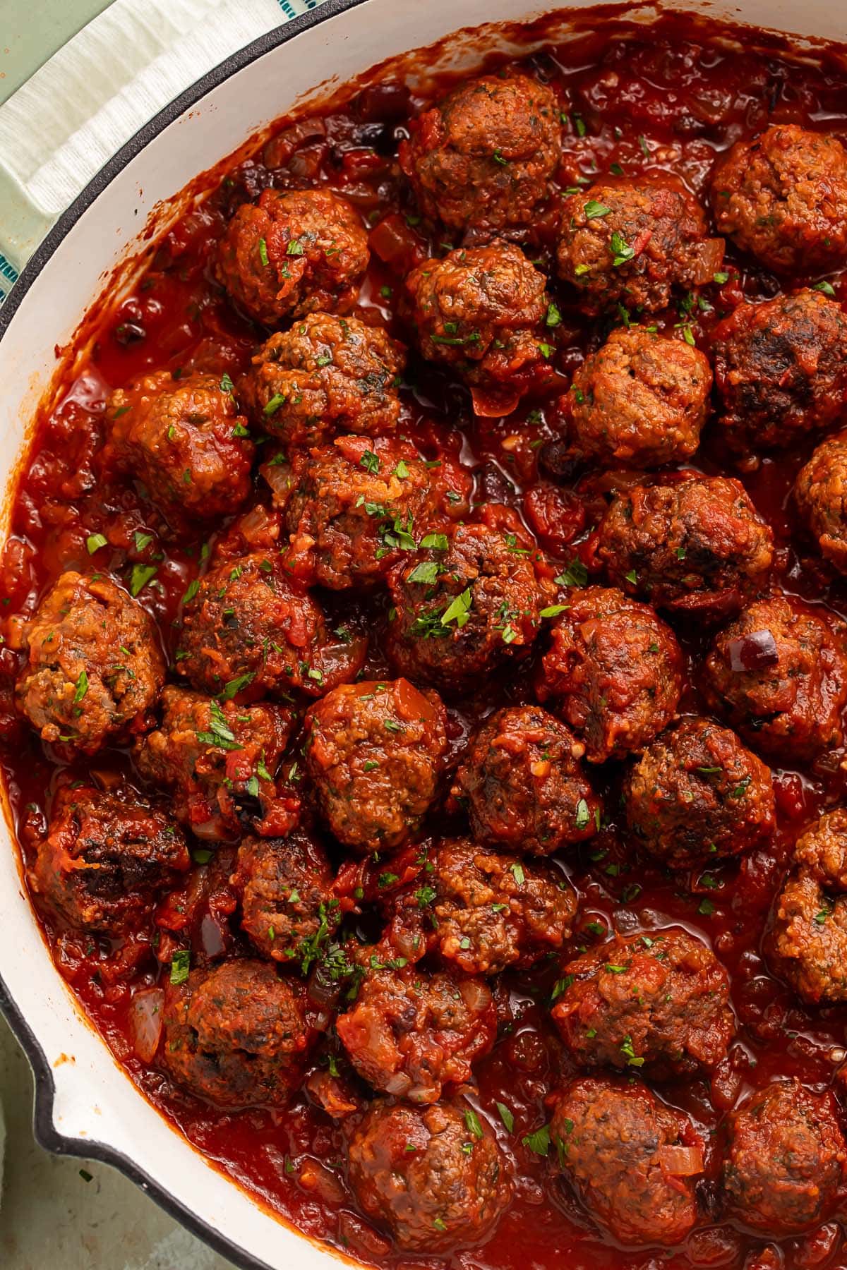 A large pan of Moroccan meatballs in a deep red sauce garnished with fresh herbs.