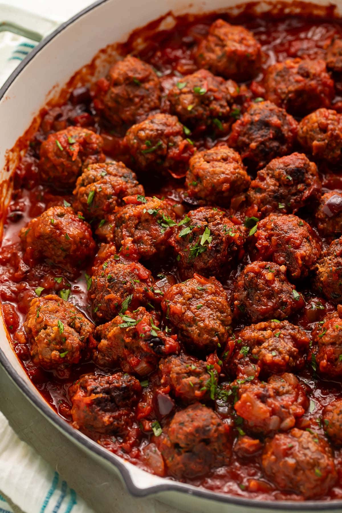A large pan of Moroccan meatballs in a deep red sauce garnished with fresh herbs.