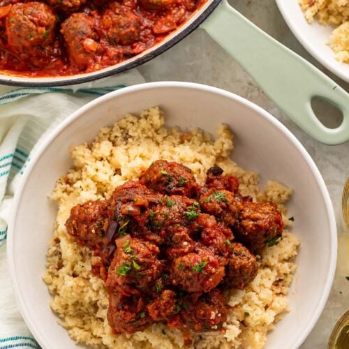 Moroccan meatballs served over a bed of fluffy couscous in a large white bowl.