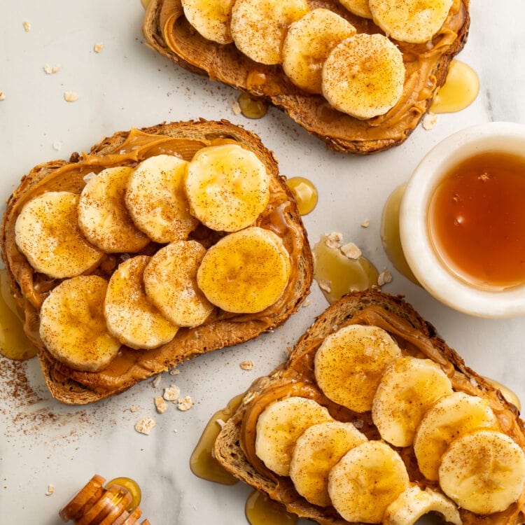 Overhead view of 3 slices of peanut butter banana toast drizzled with honey then topped with a dash of cinnamon and sea salt.