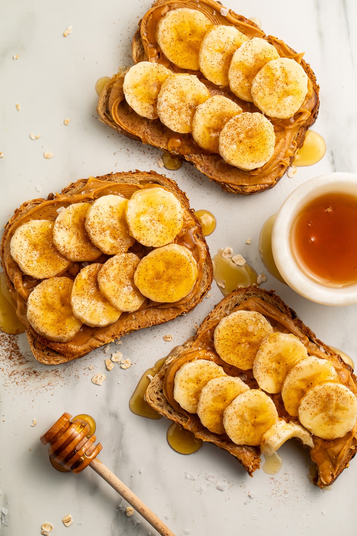 Overhead view of 3 slices of peanut butter banana toast drizzled with honey then topped with a dash of cinnamon and sea salt.