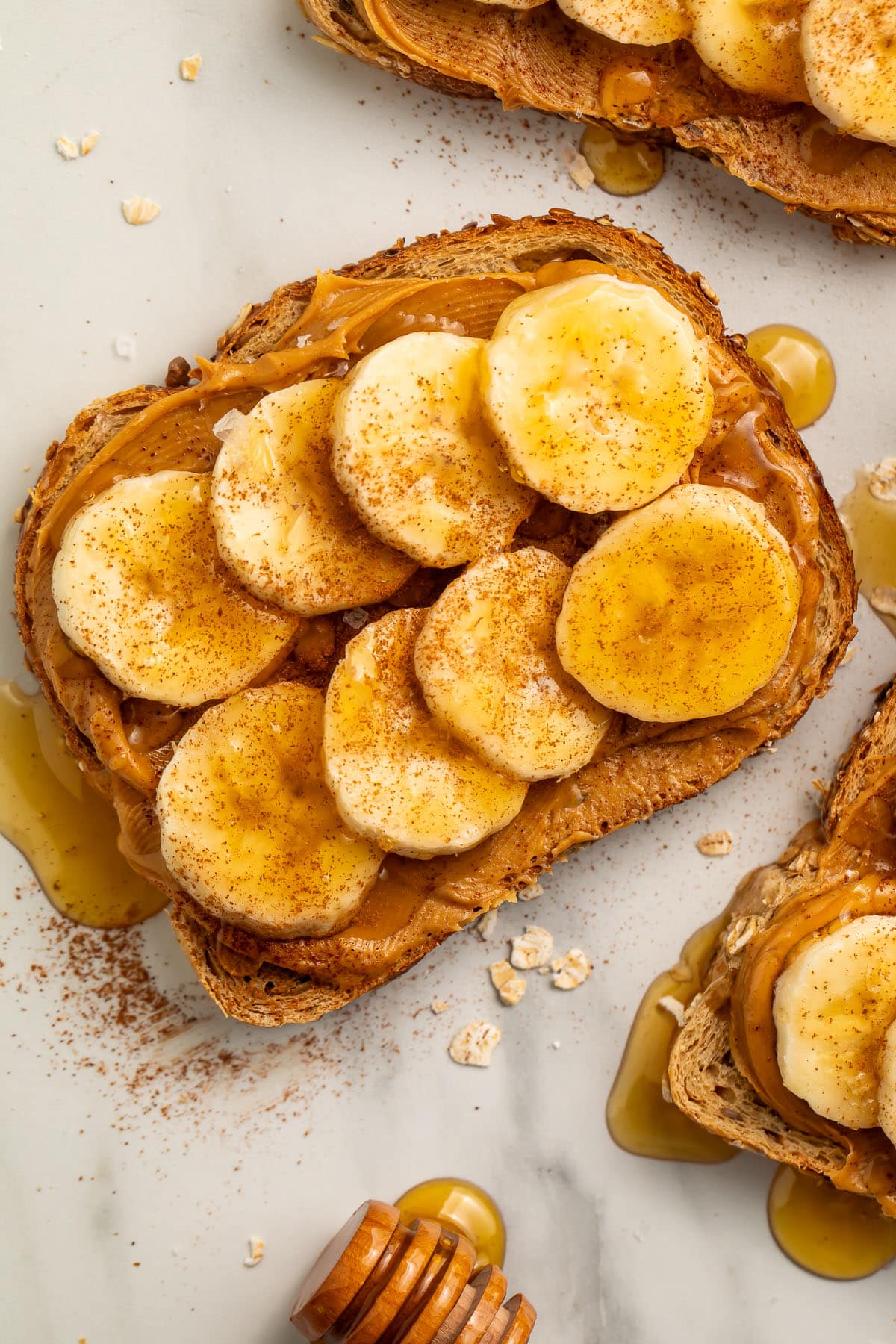 Close-up view of a slice of peanut butter banana toast topped with honey, cinnamon, and sea salt.