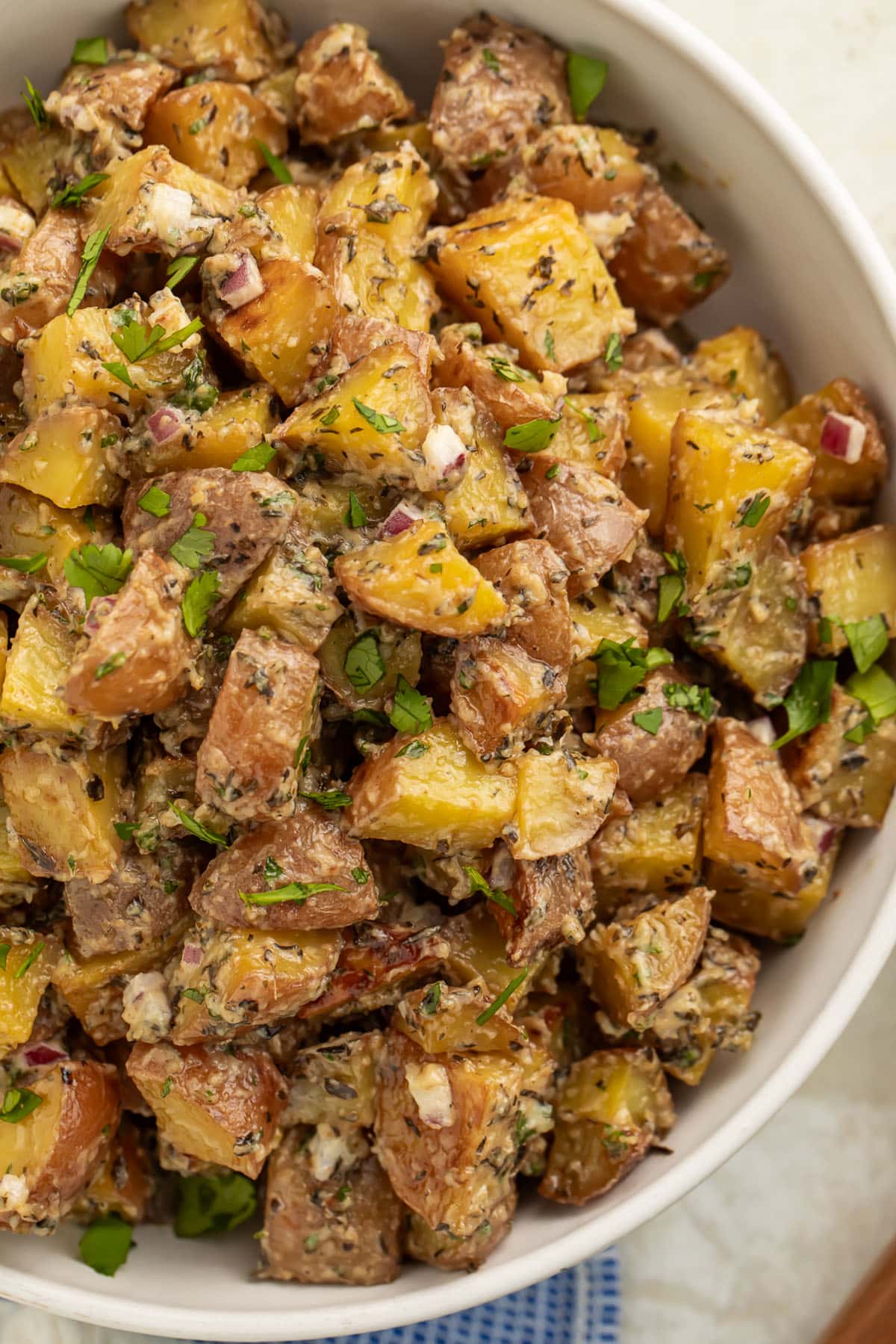 Overhead view of a large bowl of roasted potato salad with diced roasted potatoes, fresh herbs, and red onions.