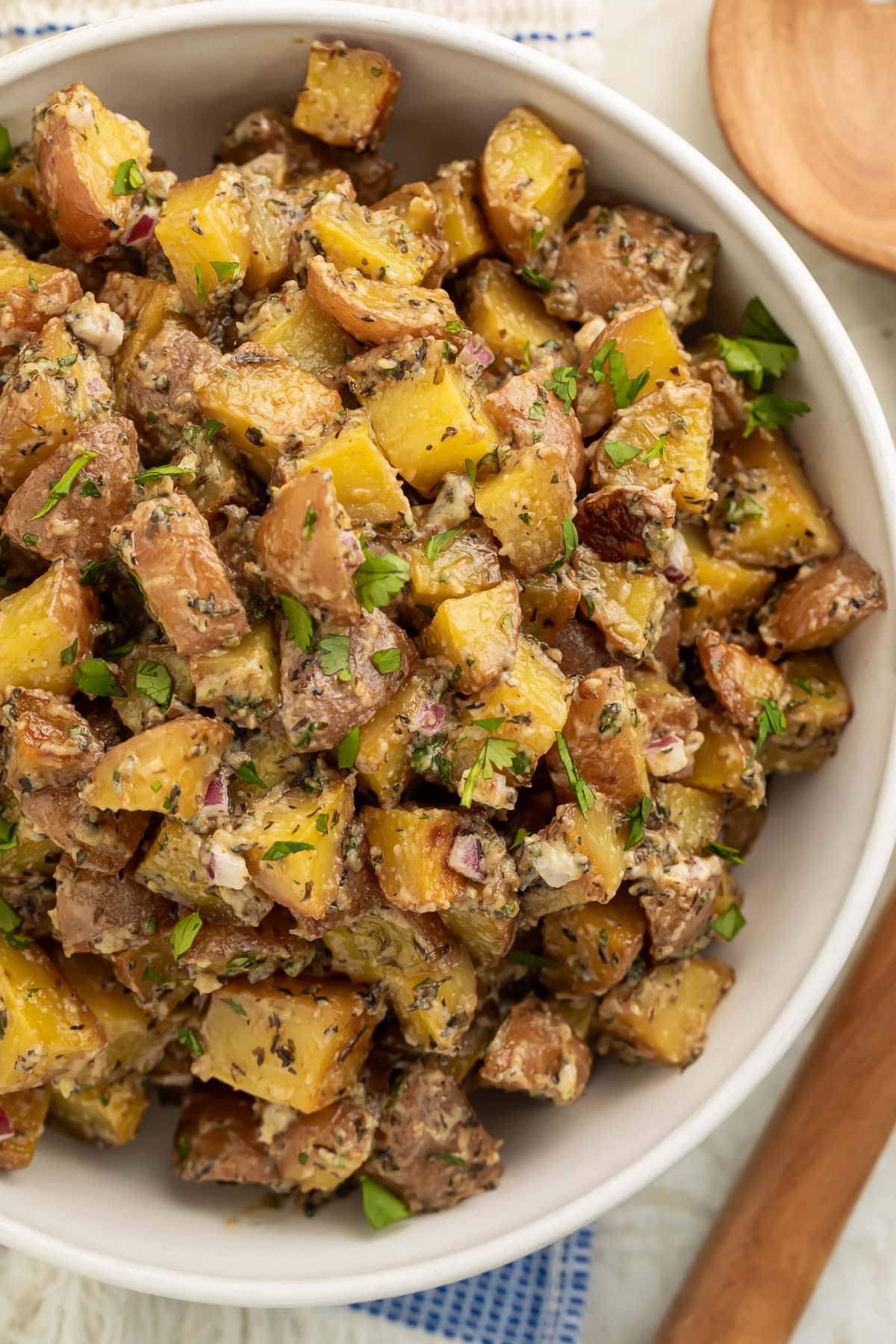 Overhead view of a large bowl of roasted potato salad with diced roasted potatoes, fresh herbs, and red onions.