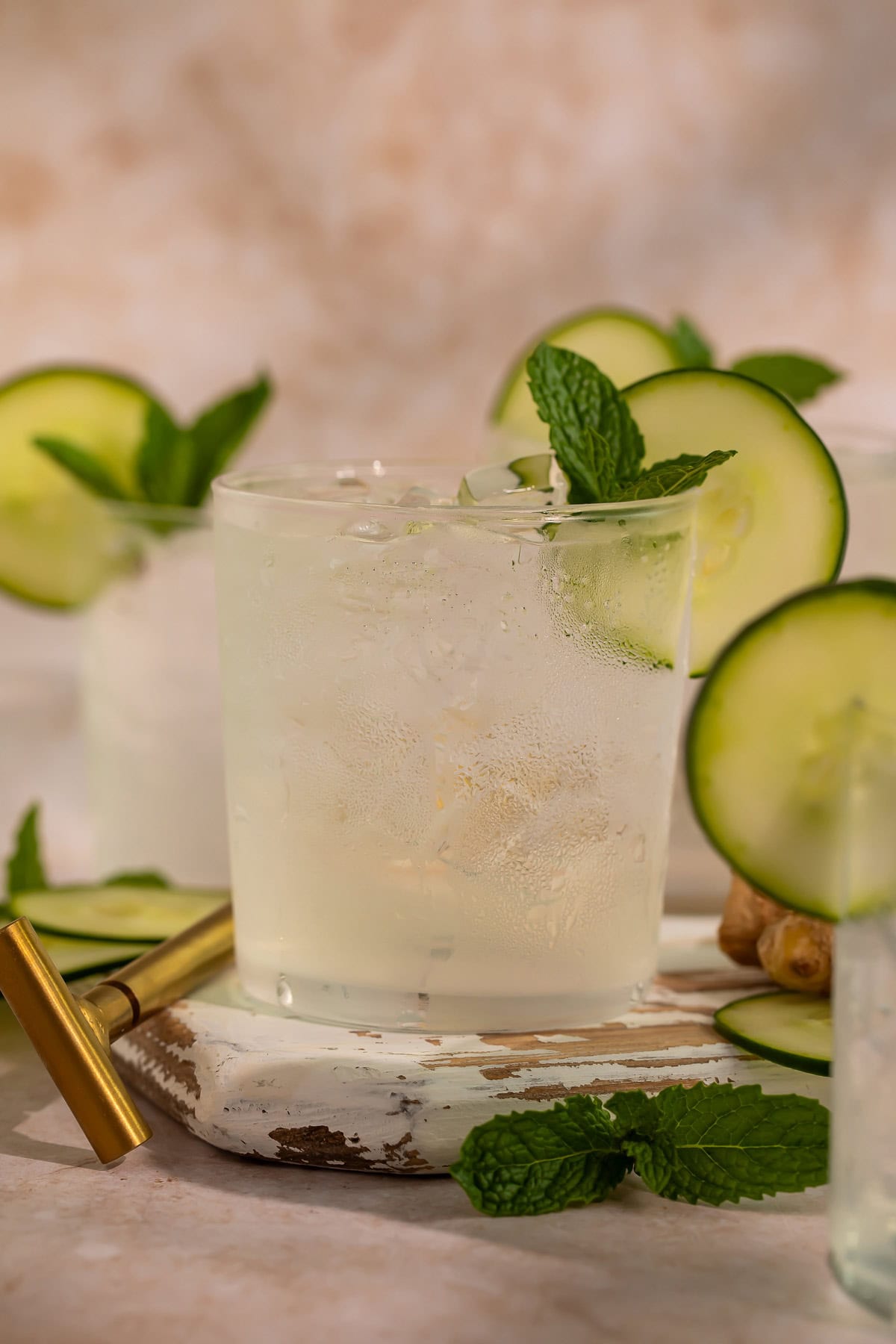 Two cucumber ginger mocktails garnished with mint leaves and cucumber discs on a wooden tray.