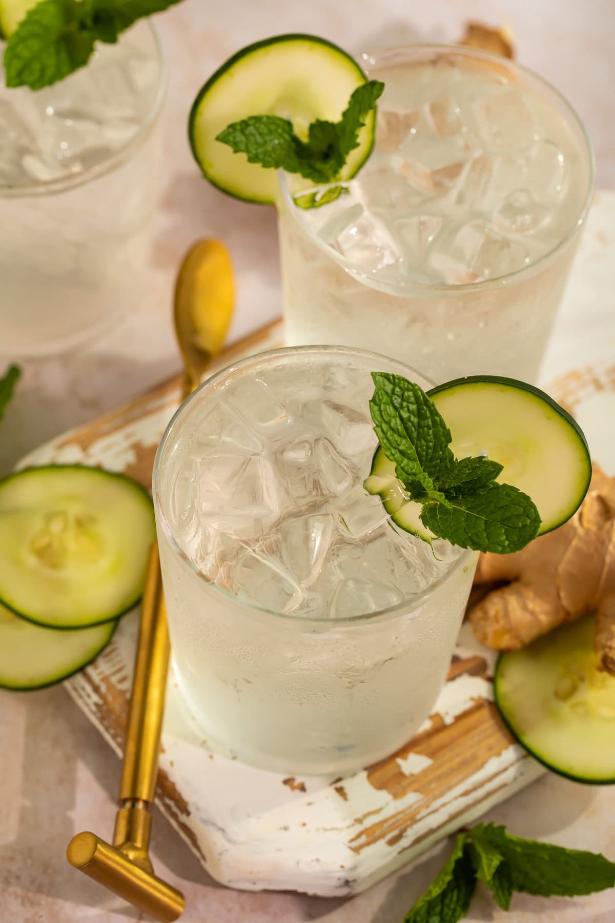 Two cucumber ginger mocktails garnished with mint leaves and cucumber discs on a wooden tray.