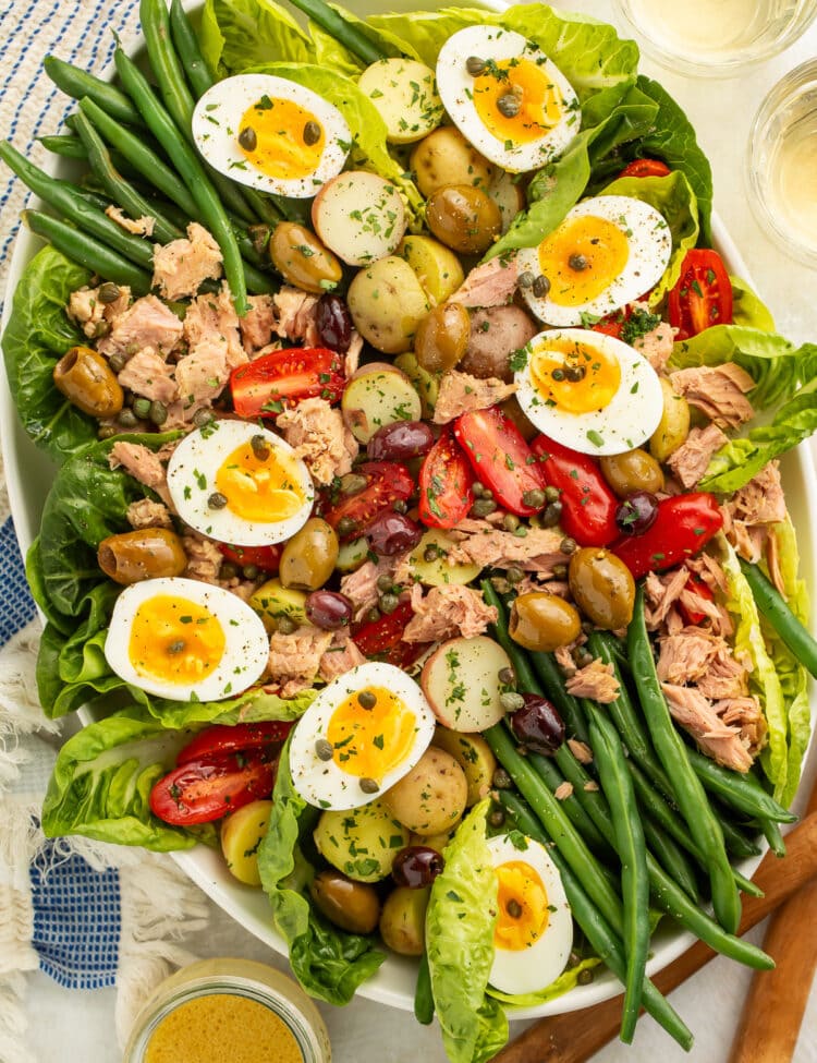 A large oval platter of Nicoise salad with potatoes, green beans, eggs, lettuce, olives, capers, tomatoes, and tuna.