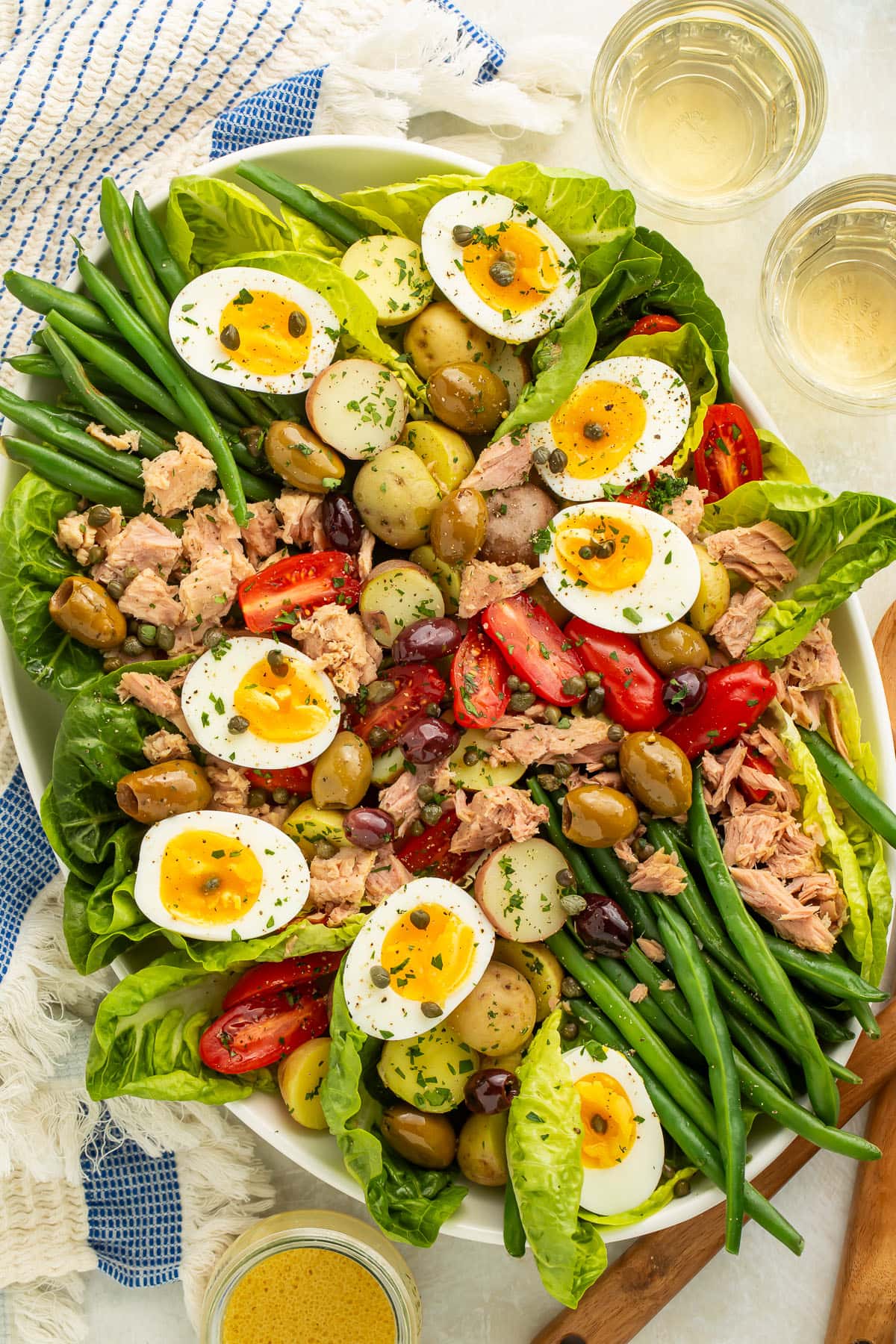 A large oval platter of Nicoise salad with potatoes, green beans, eggs, lettuce, olives, capers, tomatoes, and tuna.