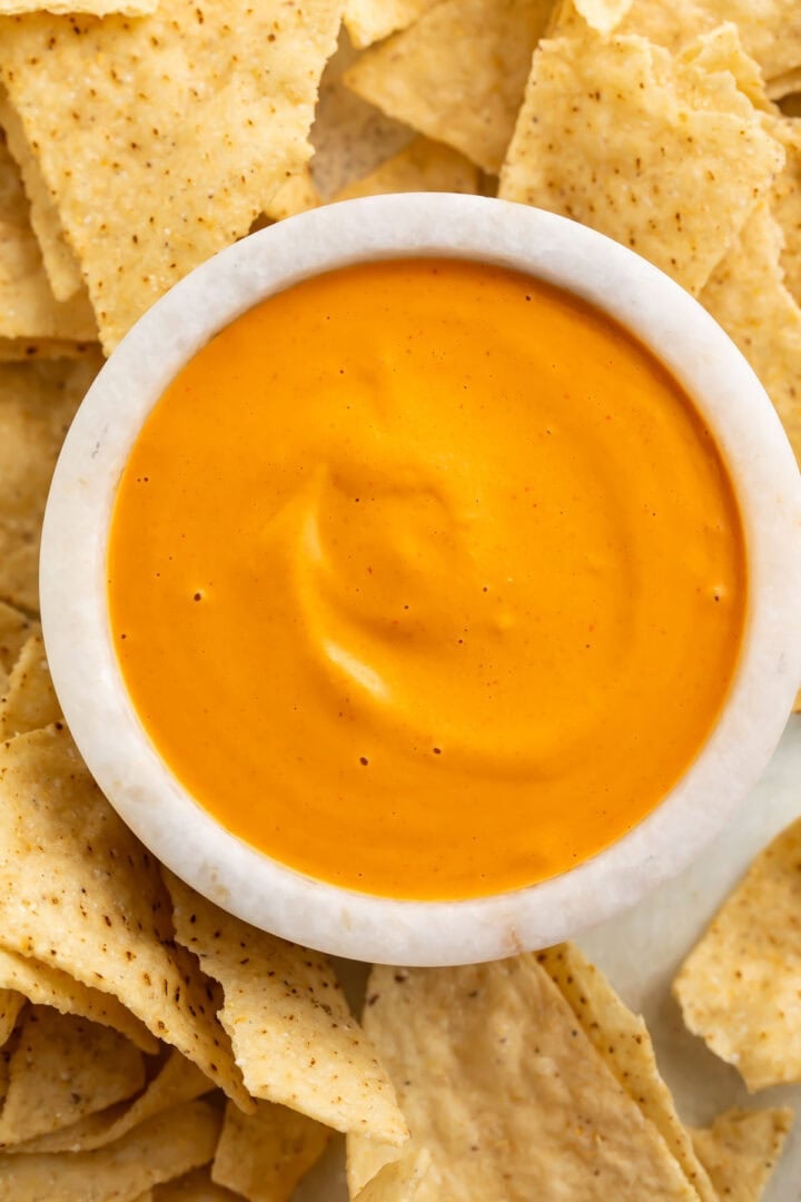 Overhead view of a white bowl of vibrant orange vegan nacho cheese sauce.