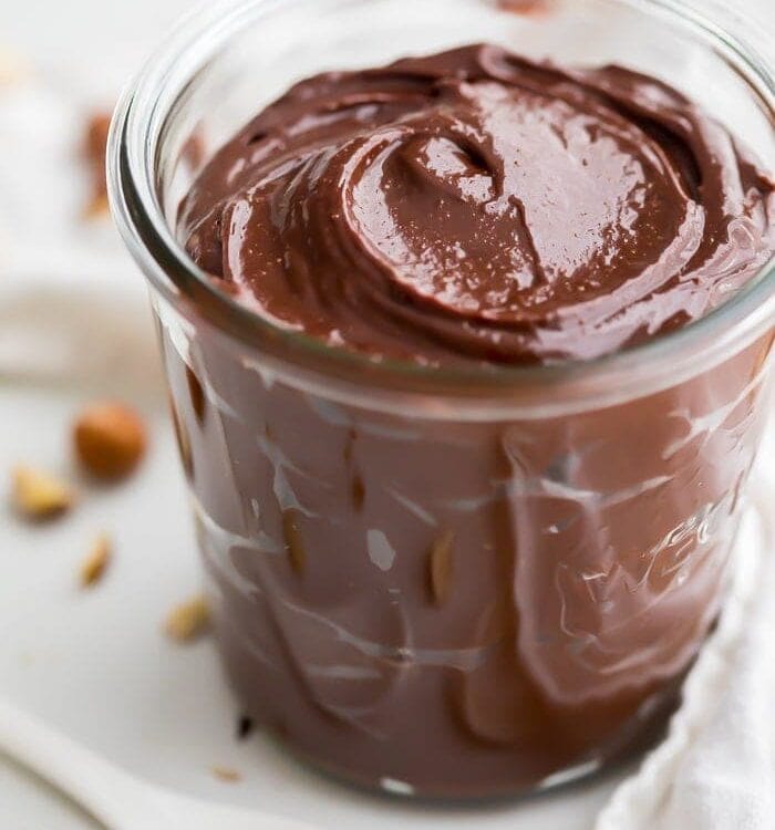 A jar of vegan Nutella with hazelnuts in the background