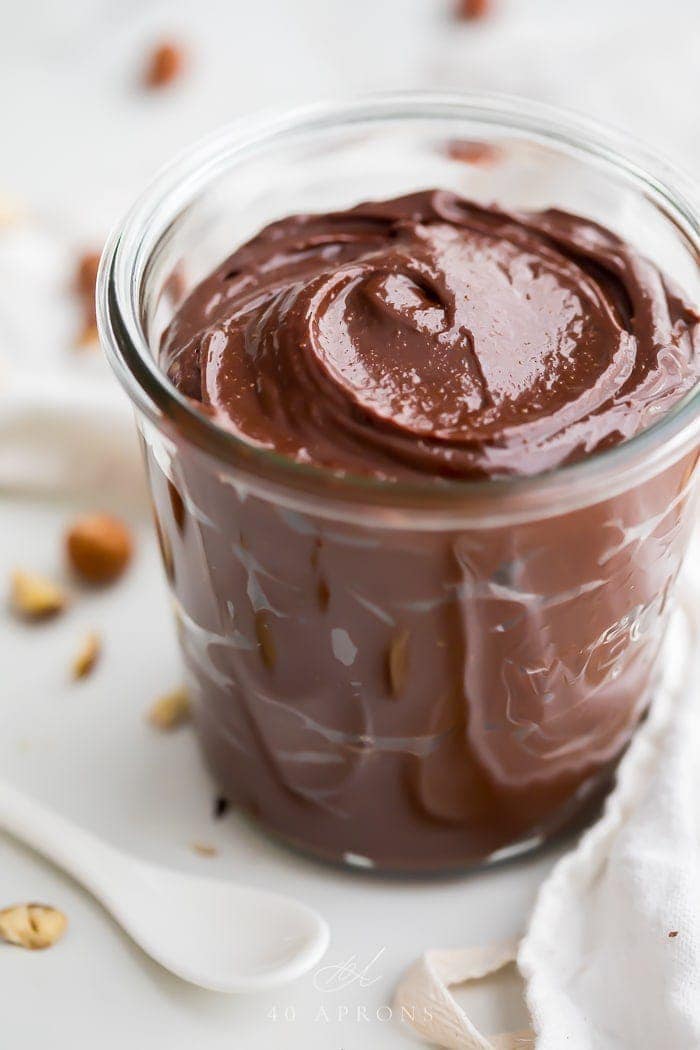 A jar of vegan Nutella with hazelnuts in the background