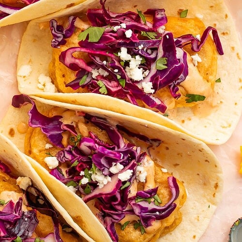 Overhead view of three beer battered tofu tacos topped with red cabbage slaw and crumbled cheese