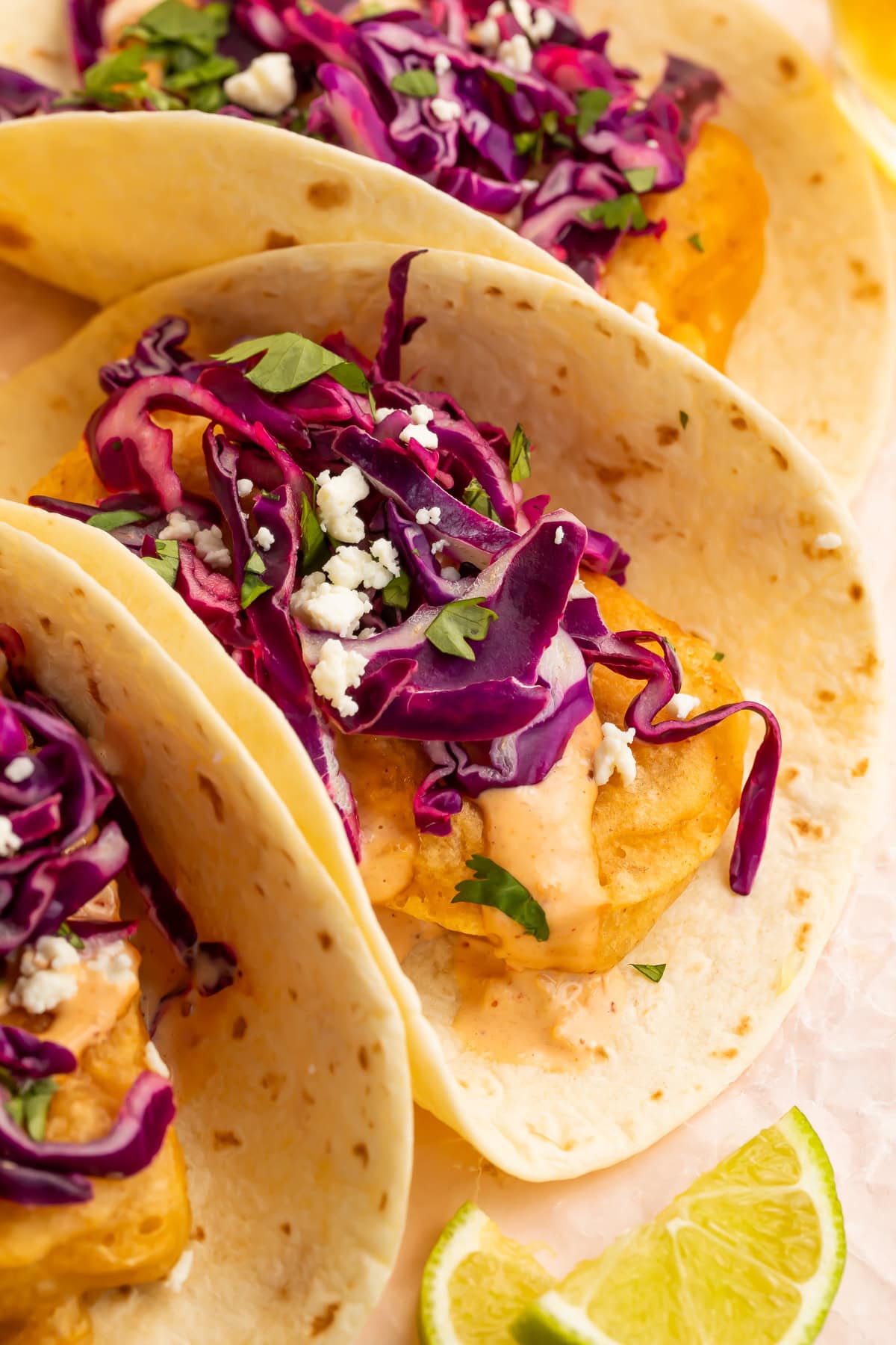 lose-up of beer battered tofu tacos with red cabbage slaw, adobo aioli, and lime wedges