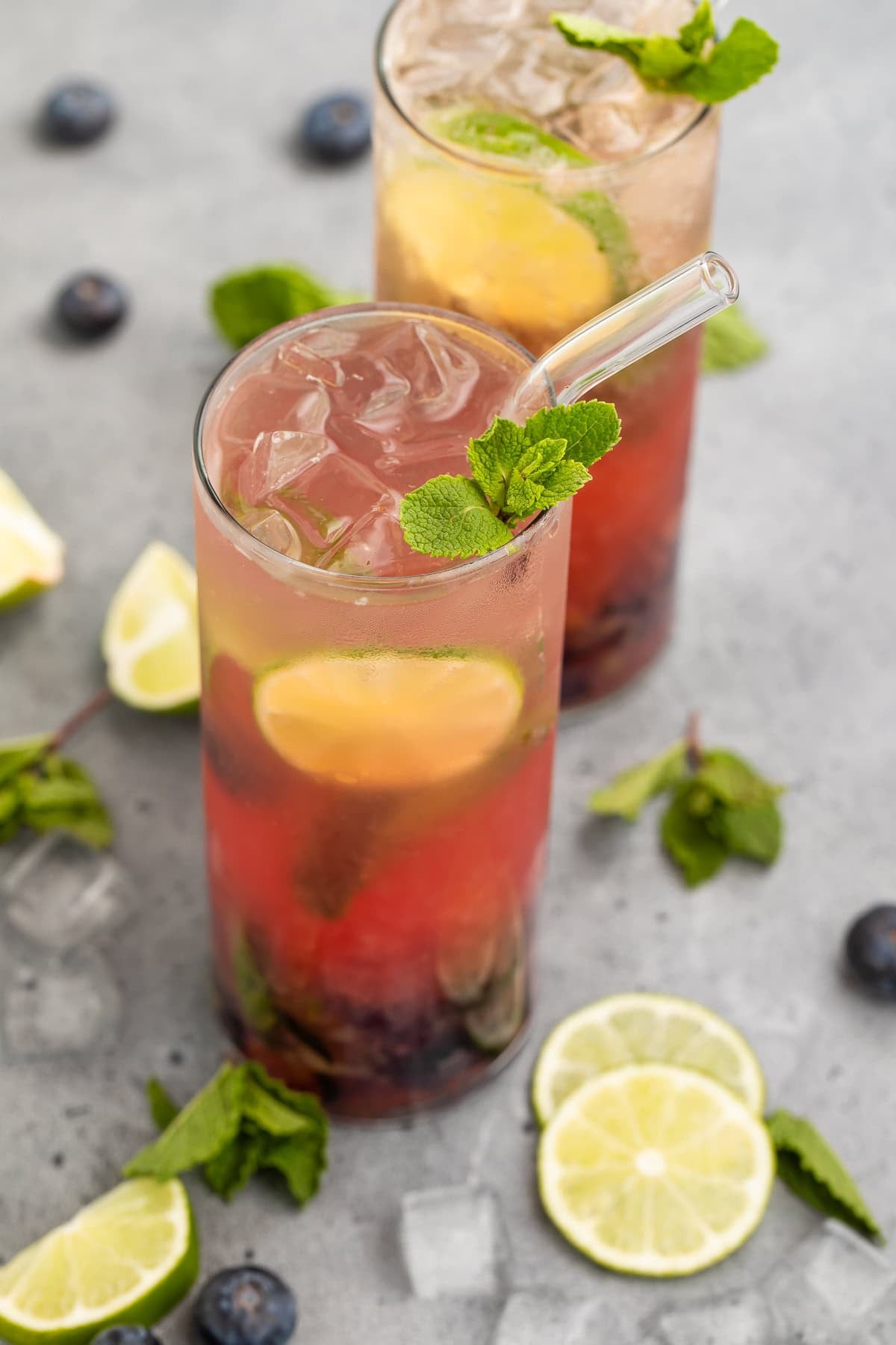 Two blueberry mojitos in a glass garnished with fresh mint and lime wheels.