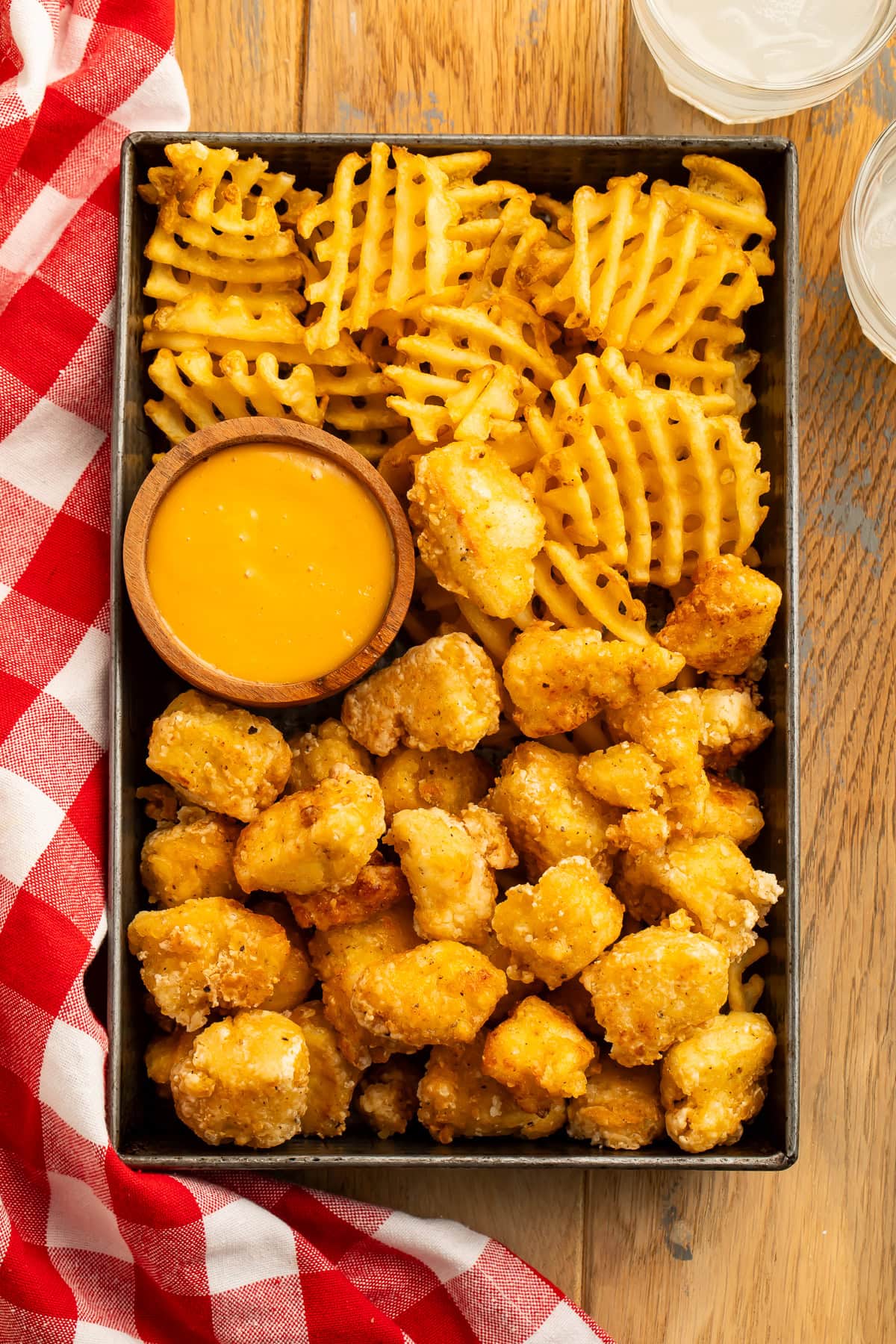 Overhead image of a metal tray of tofu nuggets, waffle fries and a honey mustard dipping sauce.