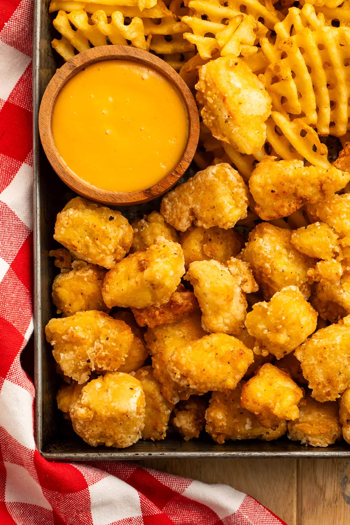 Close up of a tray of tofu nuggets and waffle fries with a pot of creamy mustard sauce.
