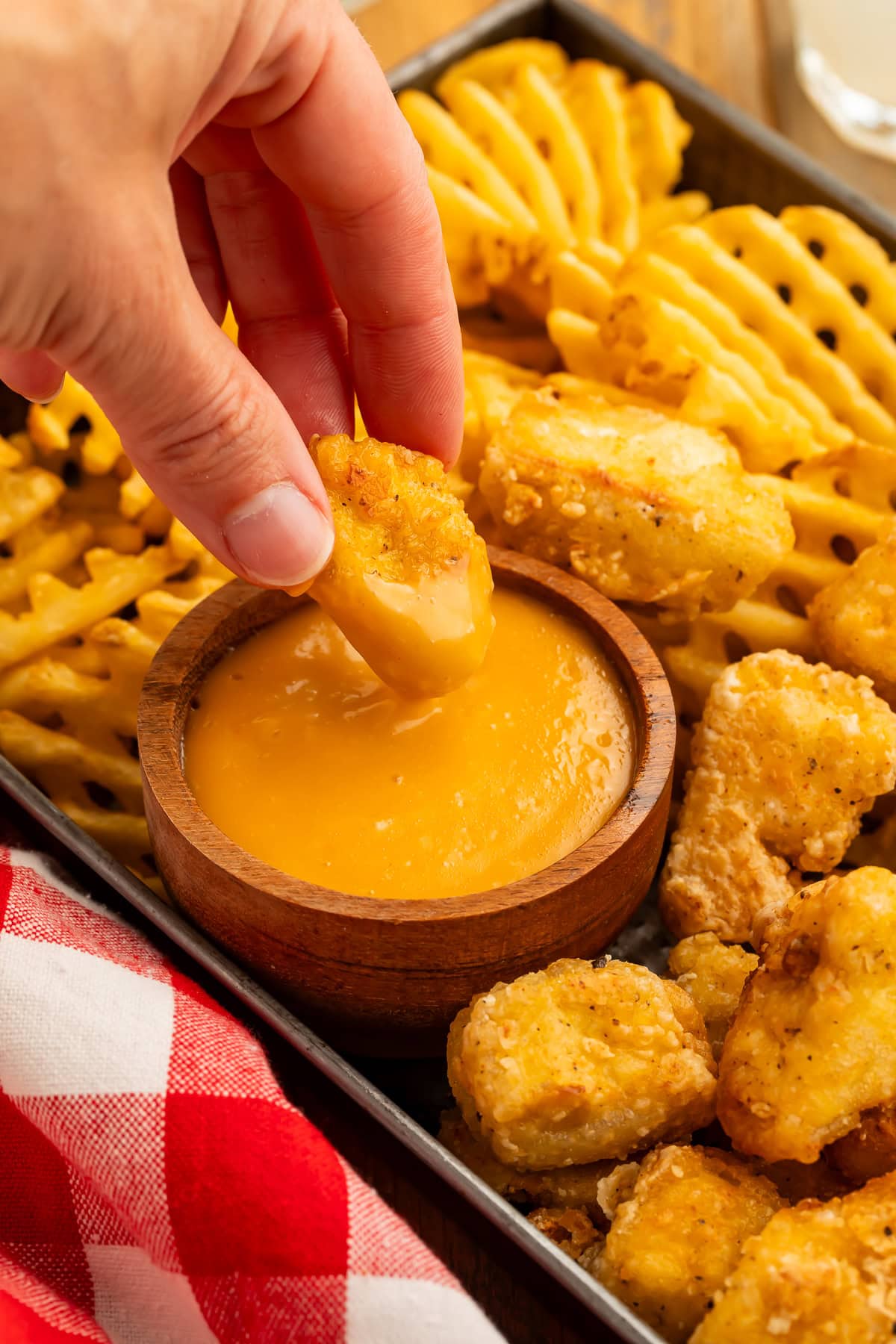 Hand dipping a tofu nugget in a creamy orange sauce.