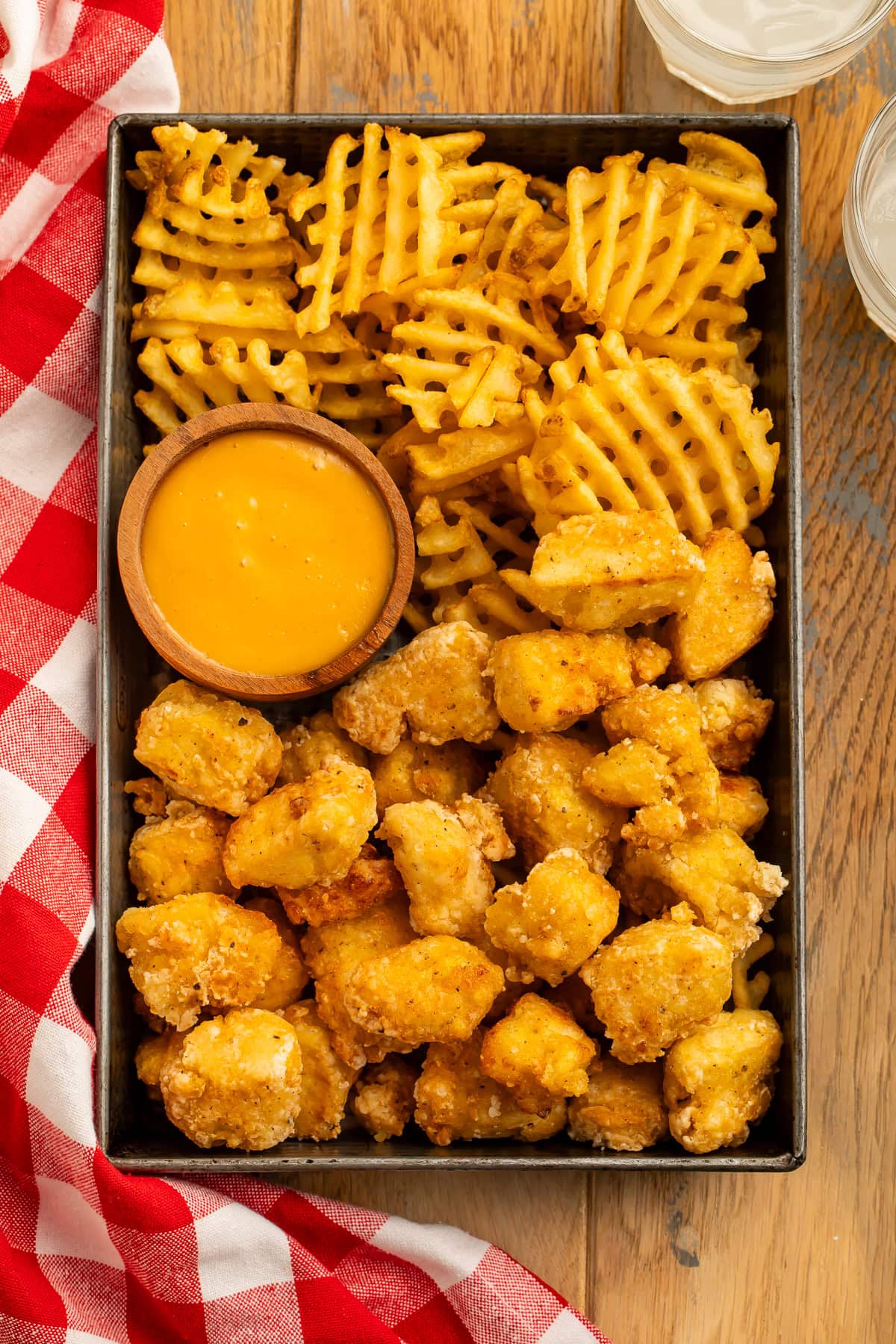 Tray of waffle fries, tofu nuggets and a wooden dipping pot of creamy orange sauce.