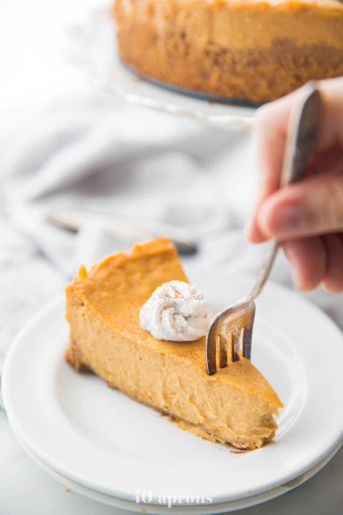 Vegan pumpkin cheesecake with whipped coconut cream on a plate with a fork cutting into it