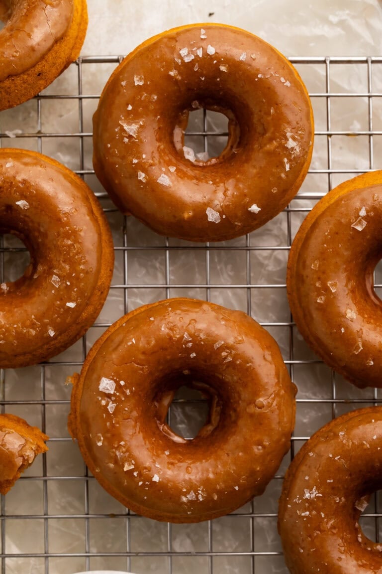 Vegan pumpkin donuts with salted caramel glaze on wire cooling rack with sea salt flakes