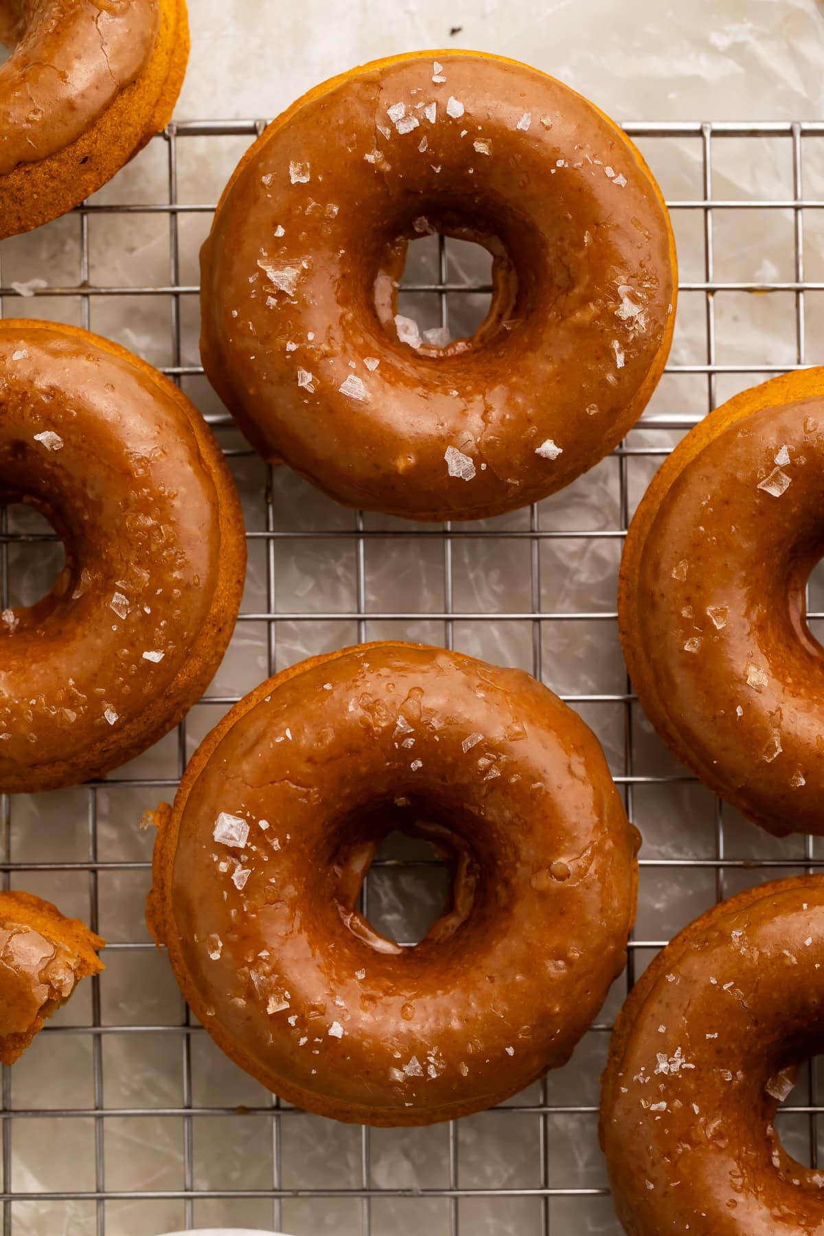Vegan pumpkin donuts with salted caramel glaze on wire cooling rack with sea salt flakes