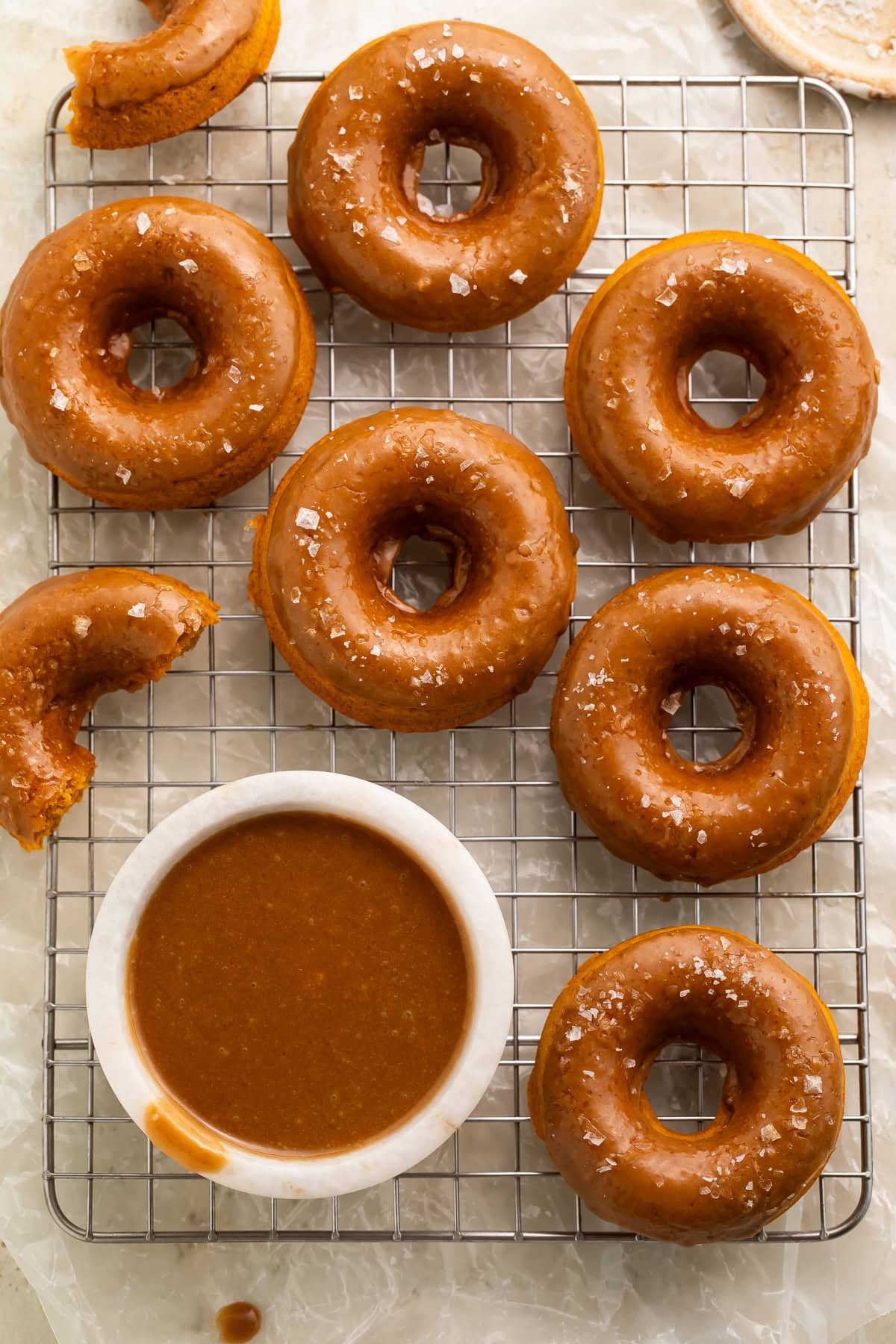 Overhead view of vegan pumpkin donuts on cooling rack with bowl of caramel sauce