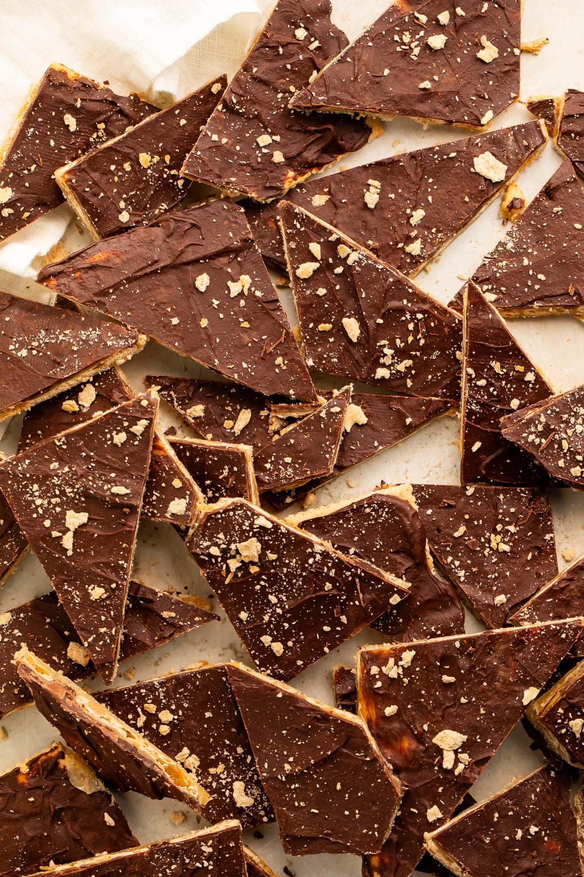 Broken pieces of saltine toffee in a pile on a piece of parchment paper.