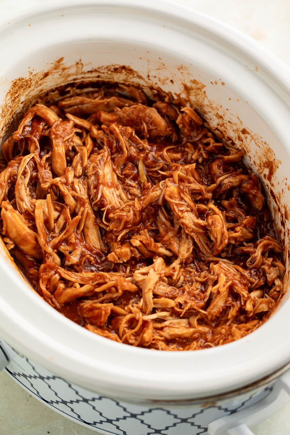 Pulled BBQ chicken in a white Crockpot sitting on a table.