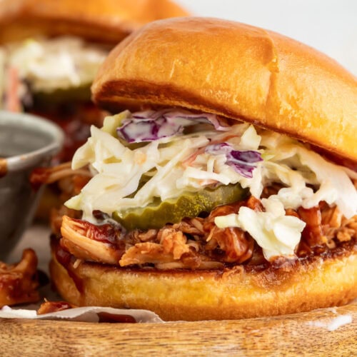 Crockpot-cooked pulled BBQ chicken on a sandwich bun with pickle chips and coleslaw.