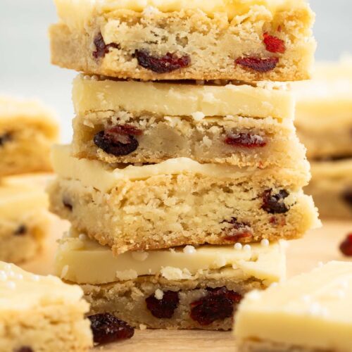 A stack of four square cranberry white chocolate cookie bars on a sheet of parchment paper.