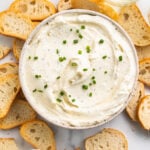 An overhead view of a bowl filled with creamy homemade boursin cheese surrounded by crisp crostini.