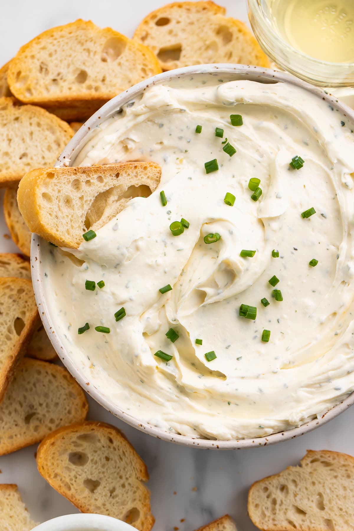 A piece of crisp crostini laying in a bowl of creamy homemade boursin cheese.