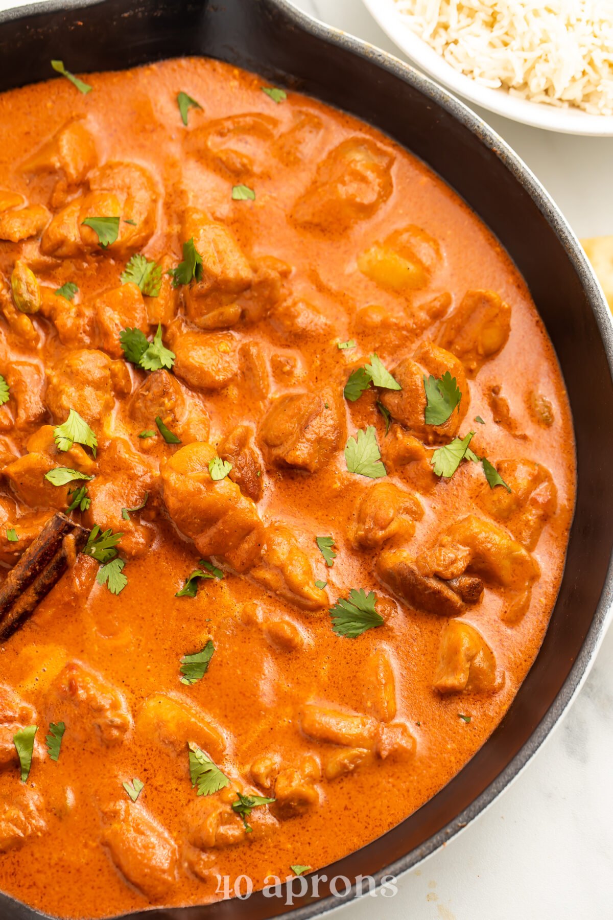 Overhead view of butter chicken in a large wok on a white countertop.